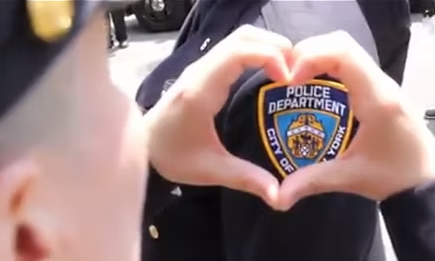 Close-up of a person forming a heart shape with their hands around a police badge.