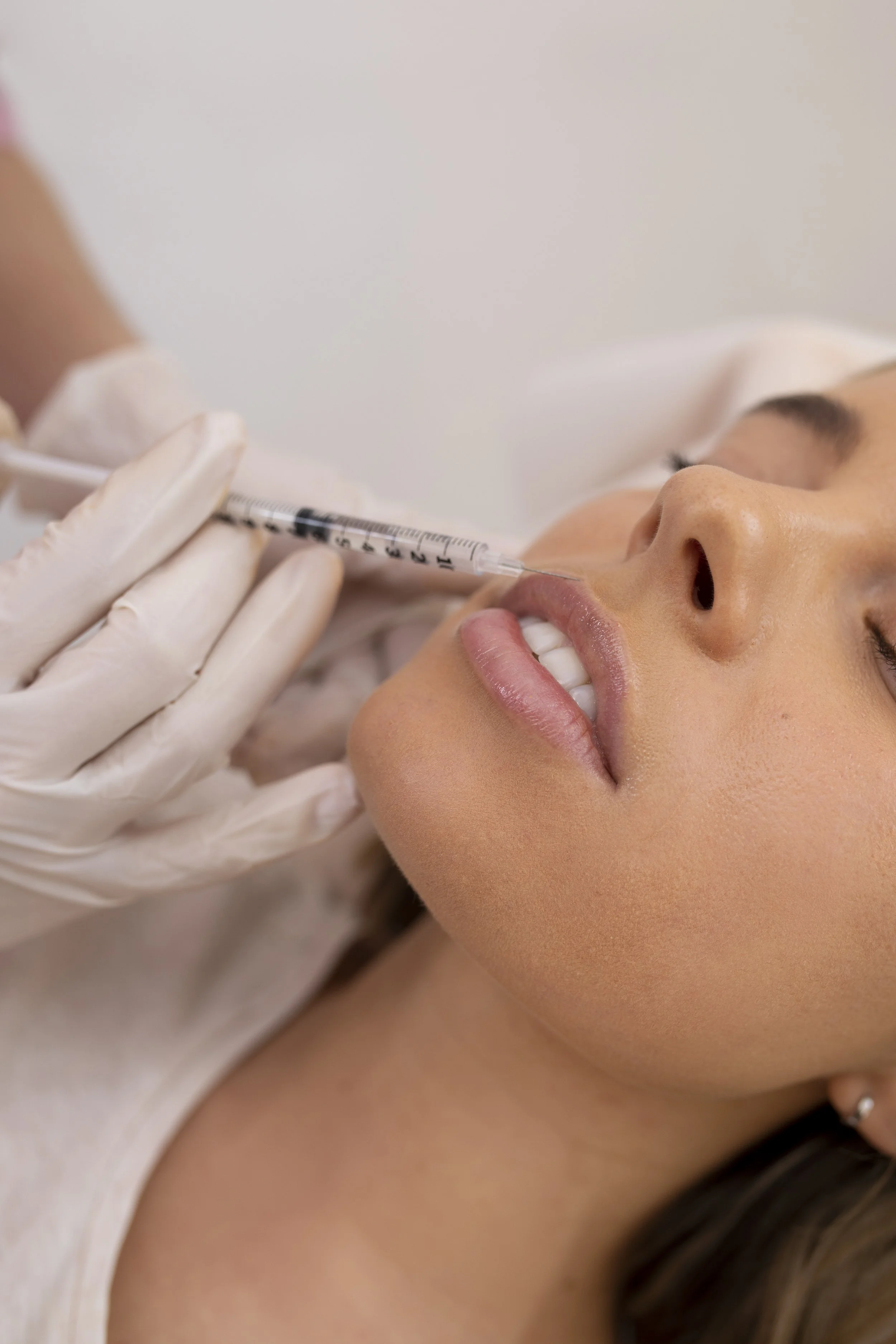 A woman receiving a cosmetic lip injection from a healthcare professional wearing gloves.