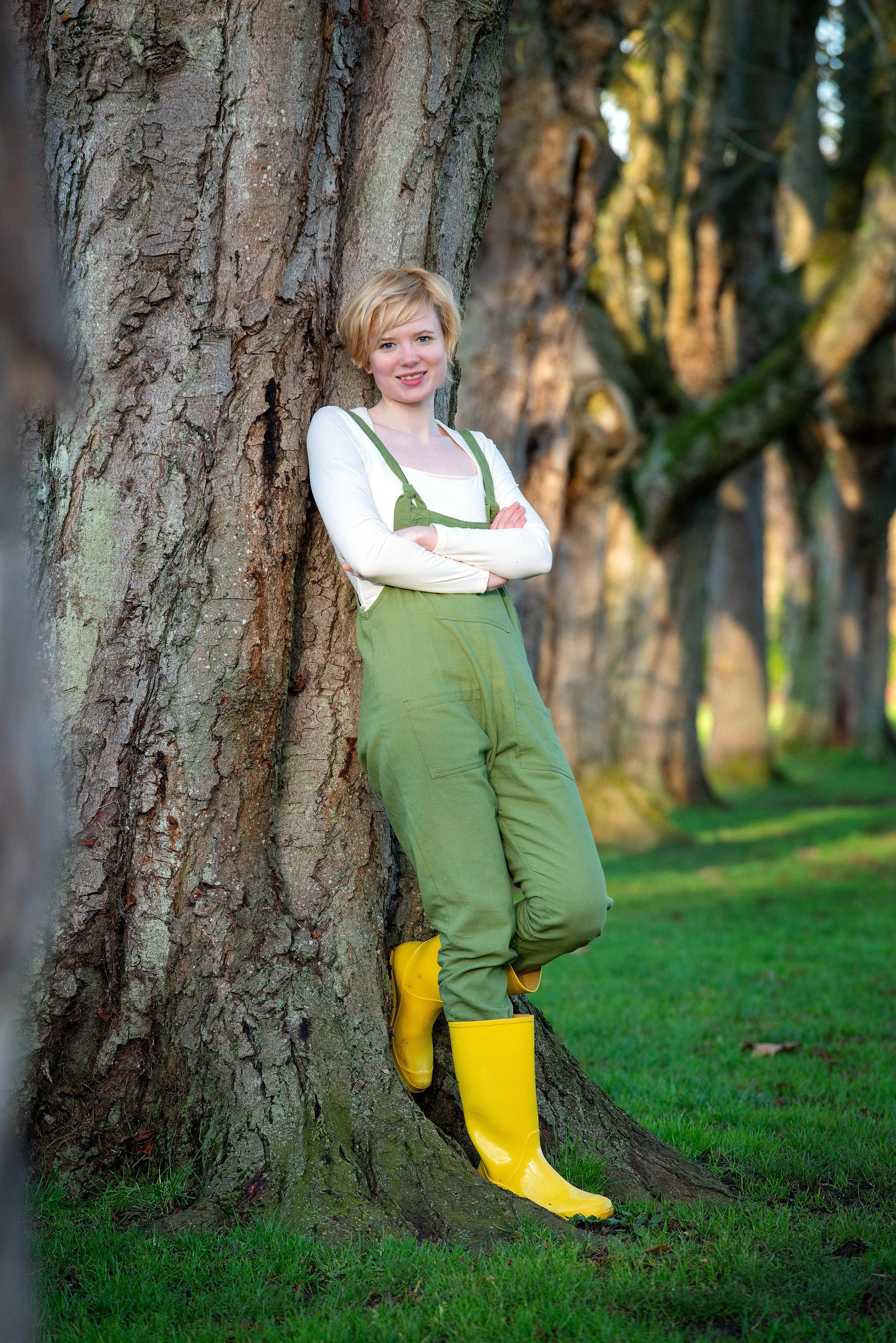 Lucy Grabe‑Watson outdoor full body portrait, leaning against a tree.