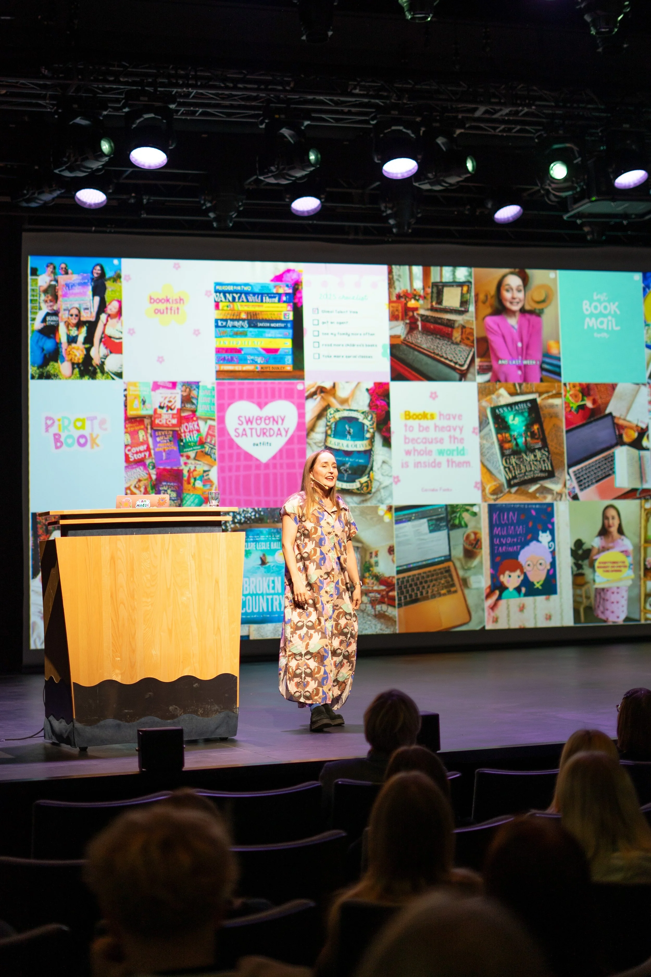 Author visit: An author speaks on stage in front of a large screen displaying various images and texts related to books, reading, and personal notes, with an audience of students watching.