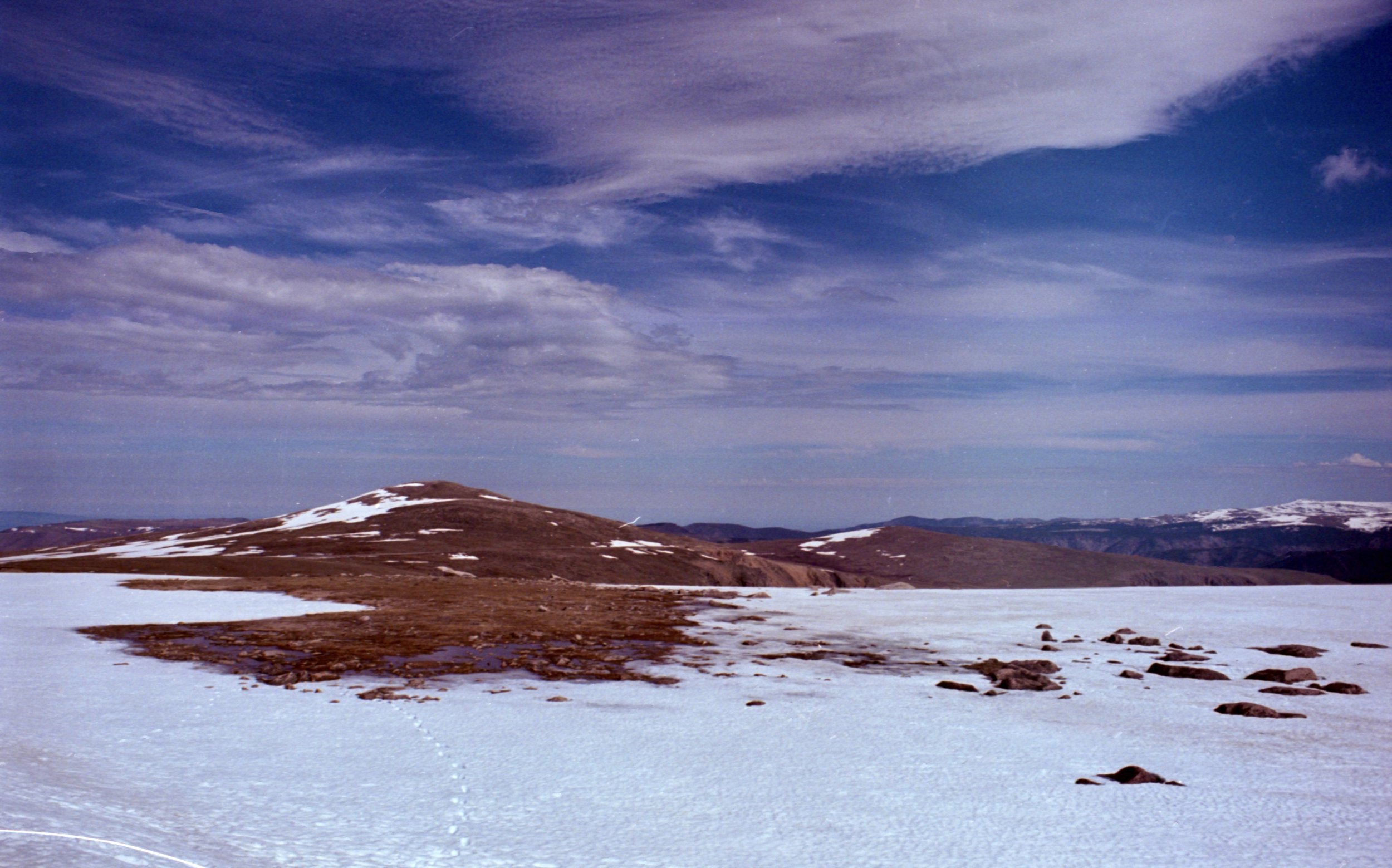 Snow-covered landscape with a mountain in the background and a cloudy blue sky.