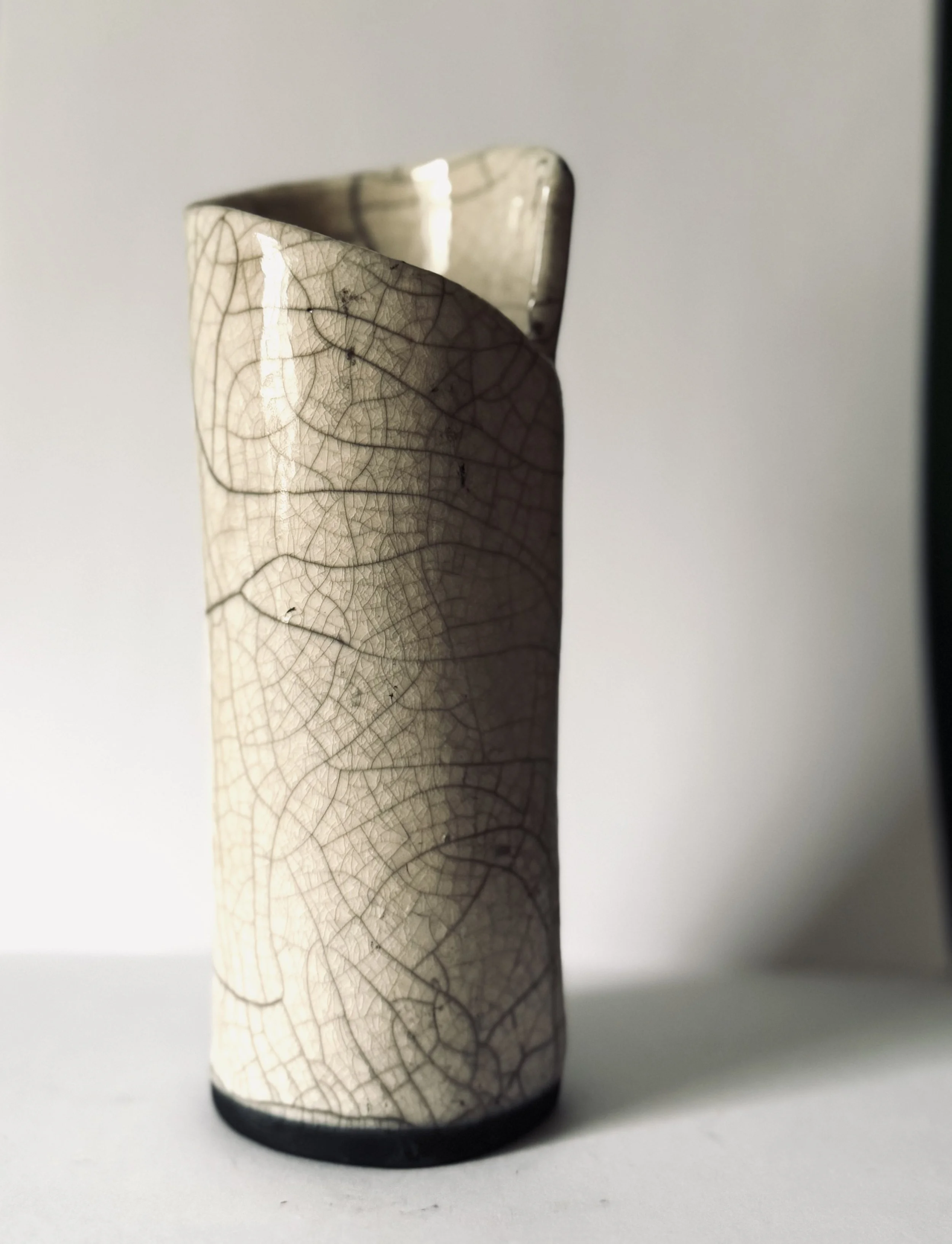 Close-up of a tall, textured ceramic vase with a crackled, leaf-like pattern, placed on a white surface against a neutral background.