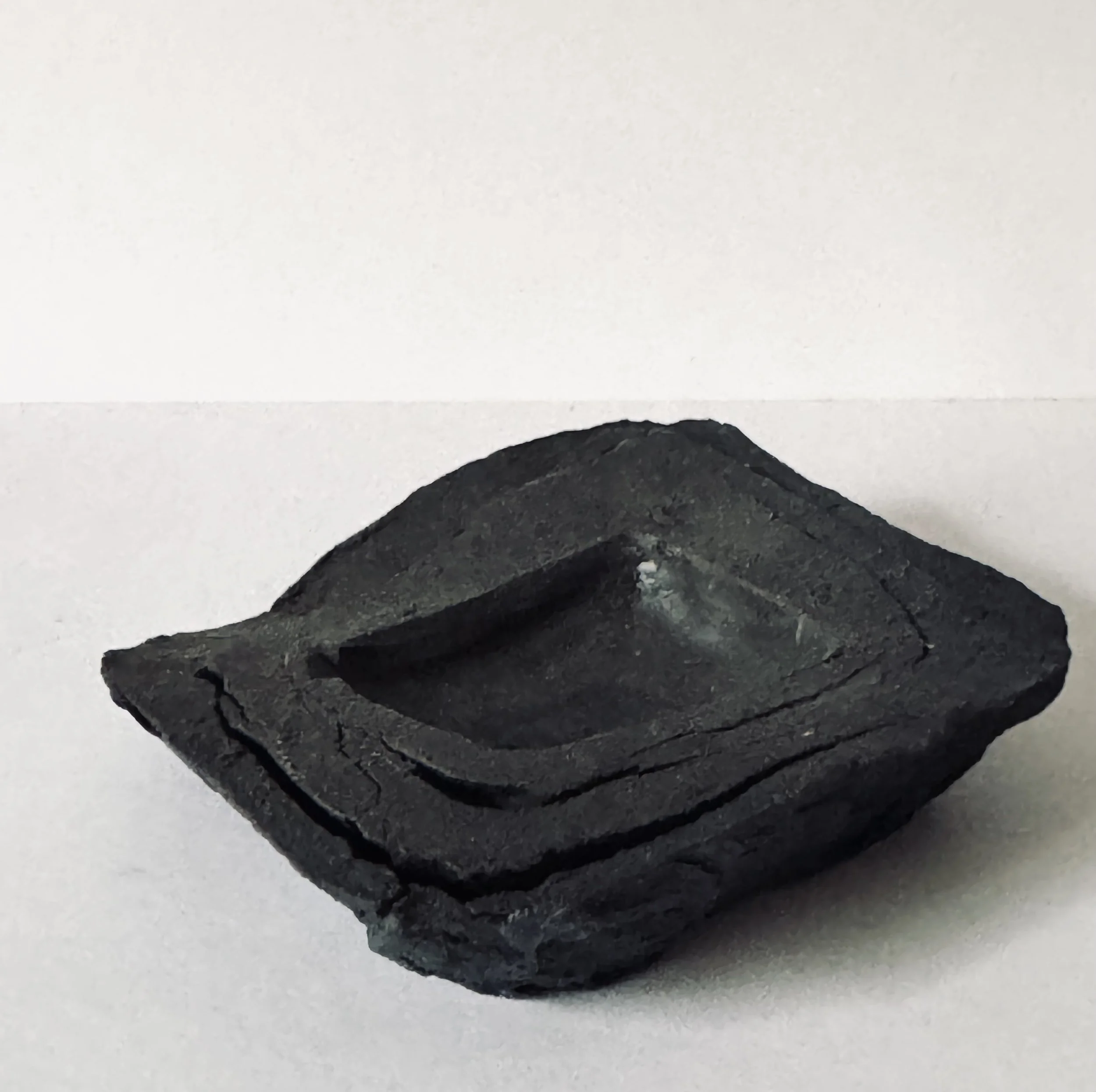 A black, irregularly shaped volcanic rock with a hollowed center, placed on a white surface.