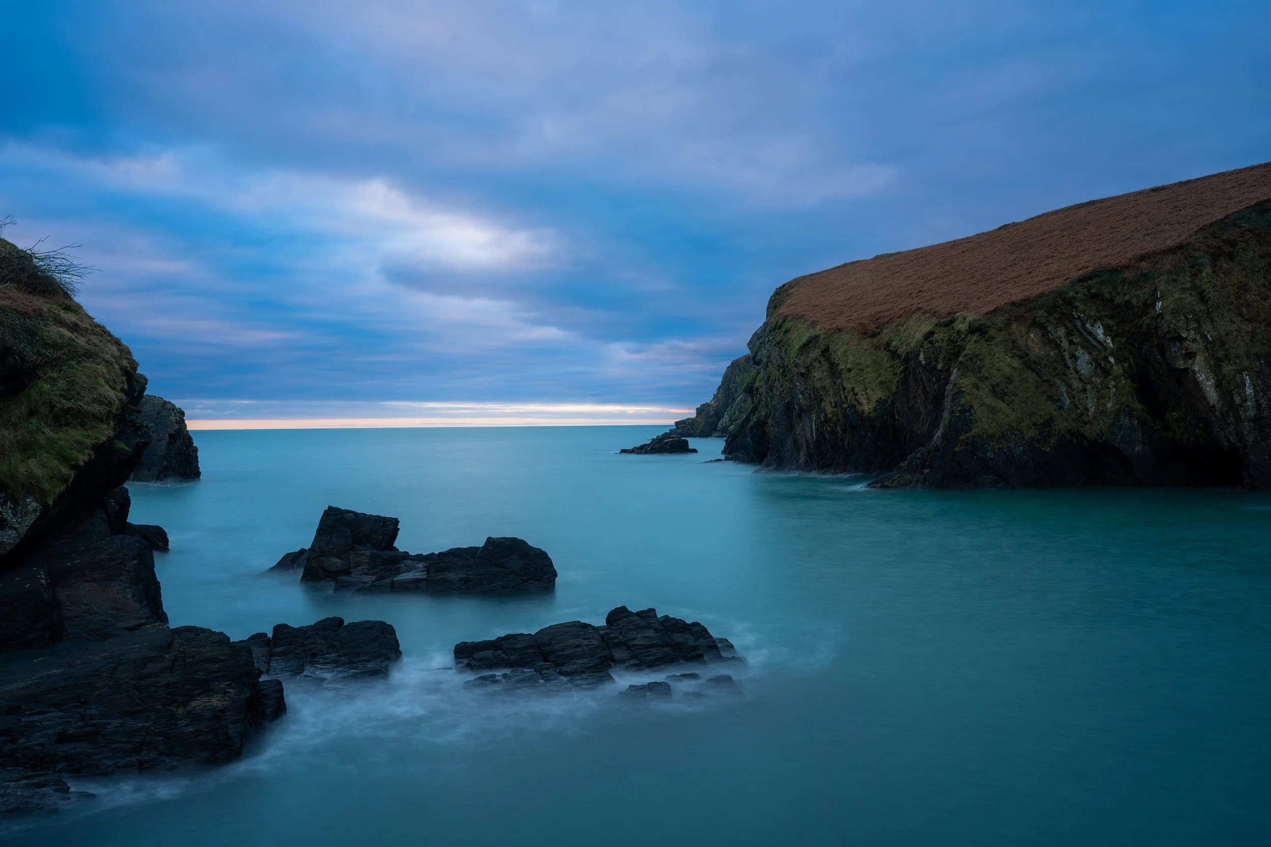 Seascape with rocky cliffs and calm ocean under a cloudy sky at dusk or dawn. Nohoval Cove 