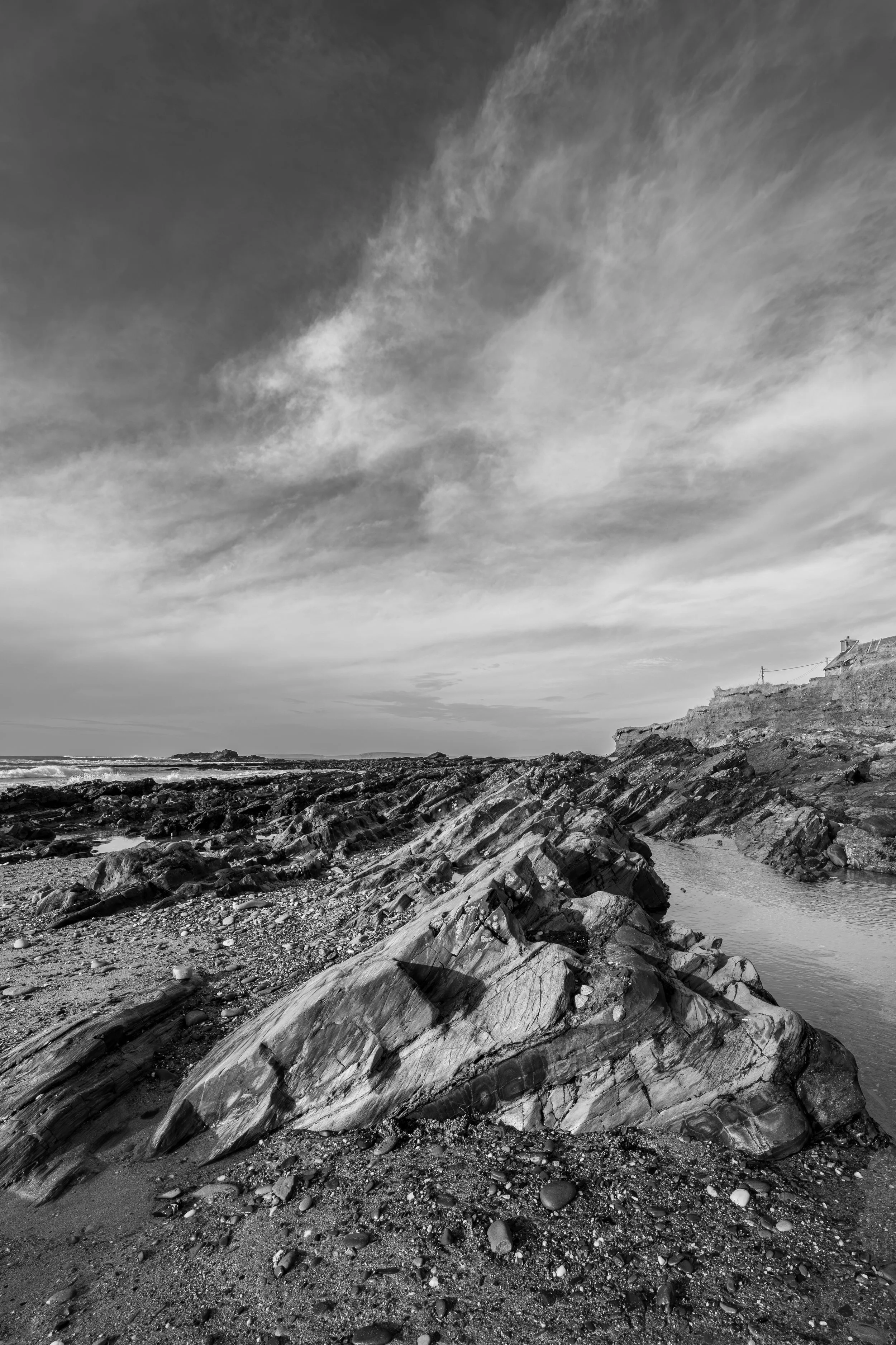 Black and white photo of a rocky beach with a cloud-filled sky above. Kinsale Cork
