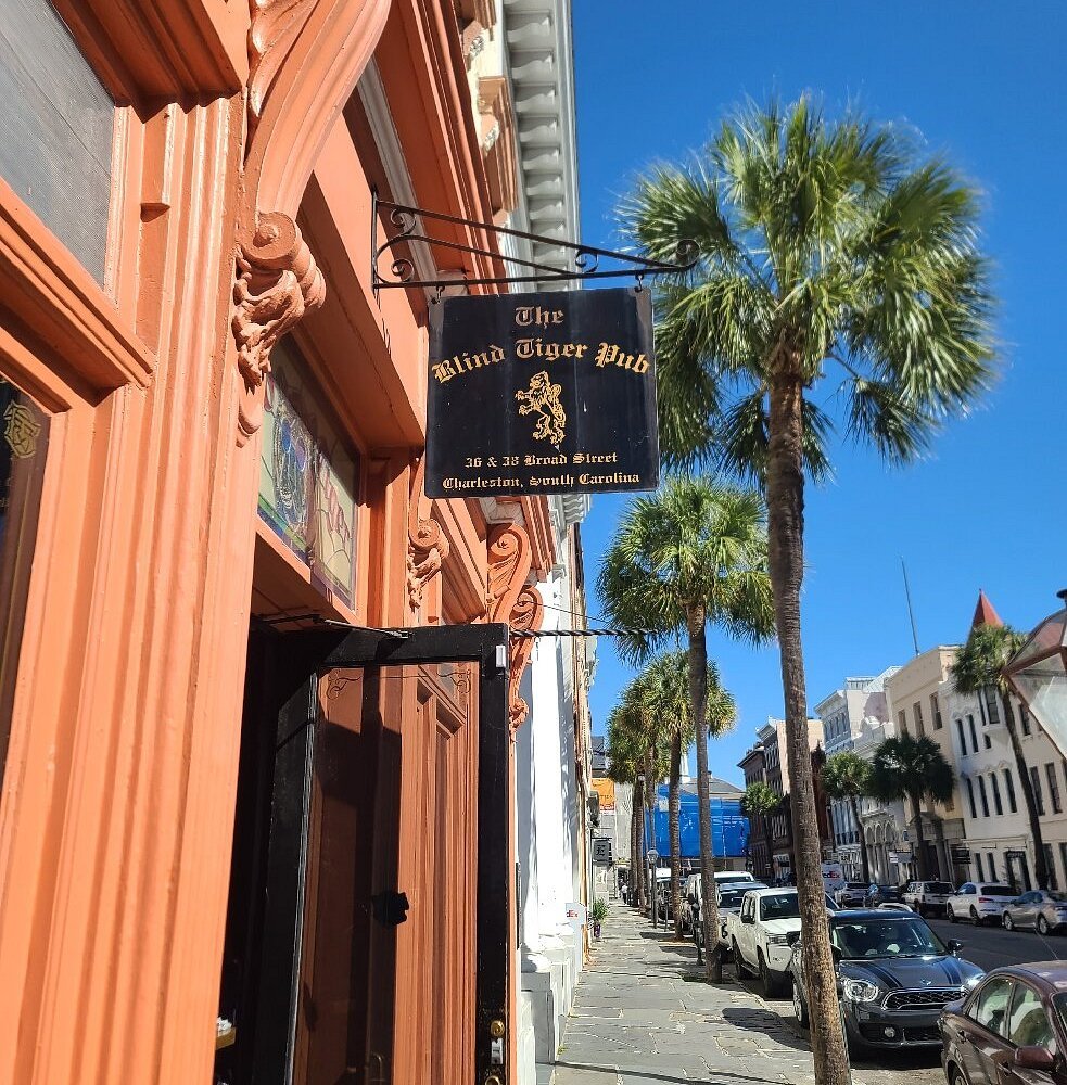 Outdoor patio of a restaurant or bar with wooden flooring, string lights, and tables and chairs. Some people are sitting and talking, and a mural of a butterfly is visible on the wall.