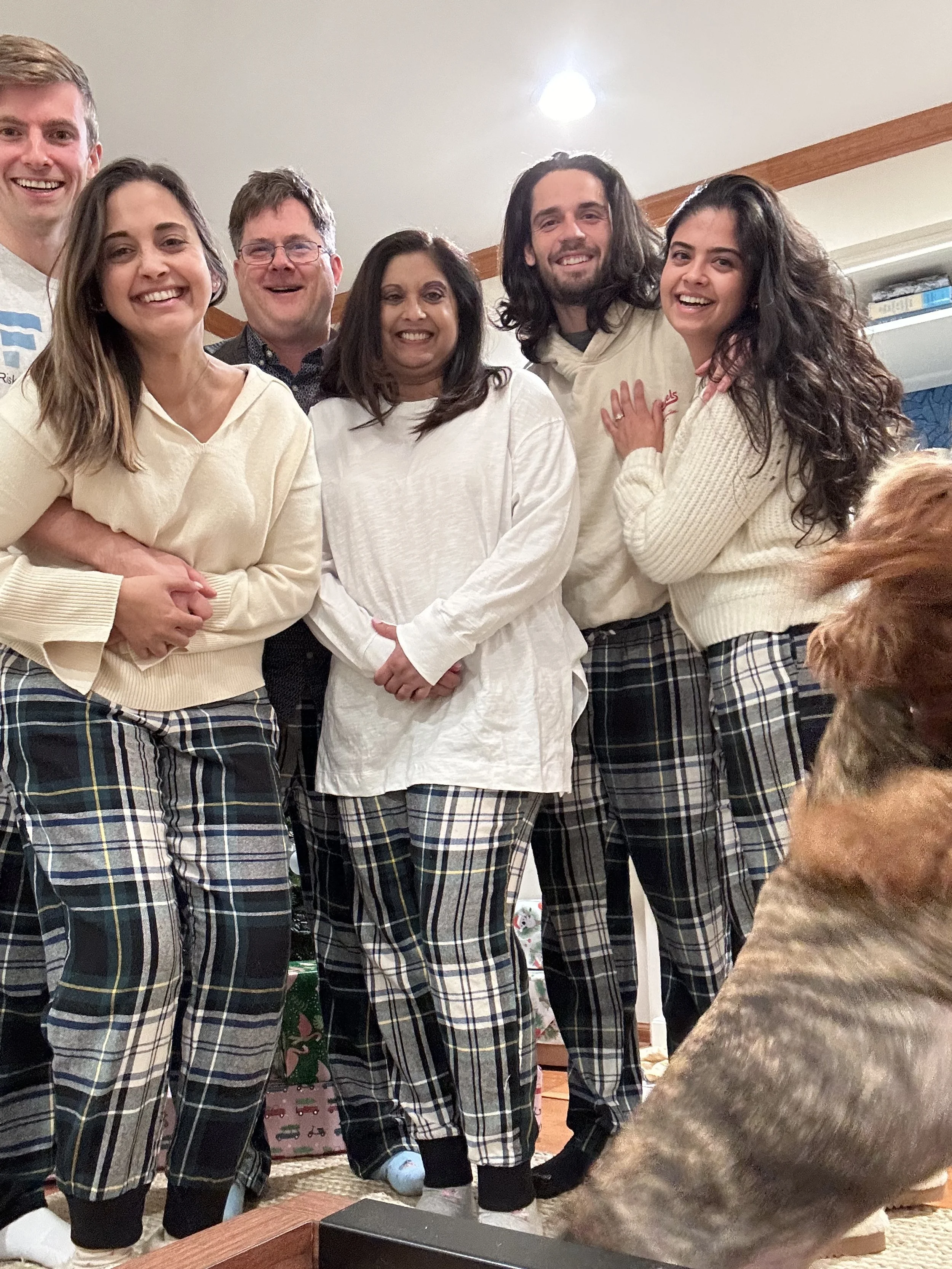 Group of six people wearing plaid pajamas smiling together indoors at night.