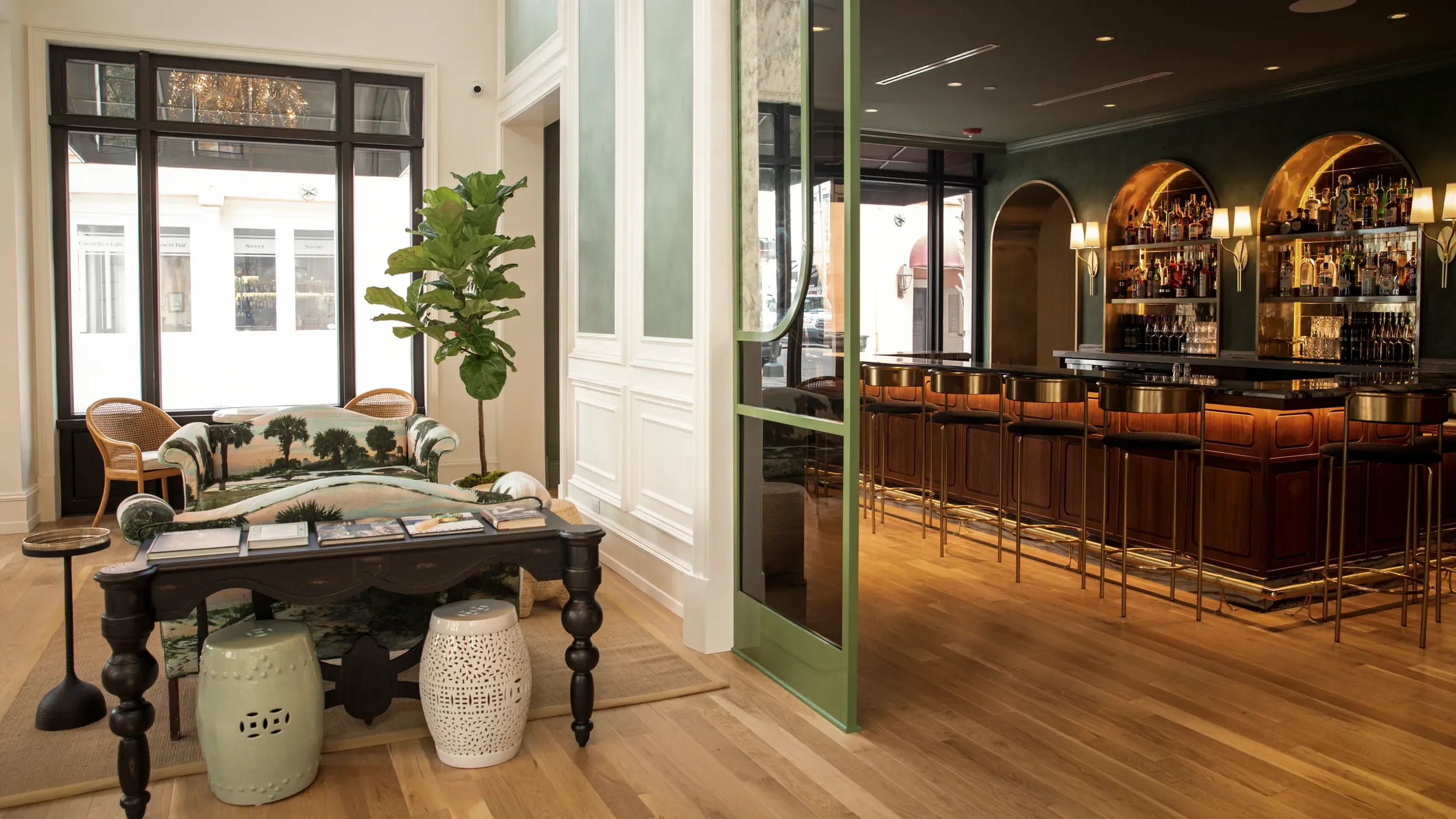 Elegant lounge bar with pink and blue armchairs, marble tables, a pink marble bar counter, floral decor, and a large crystal chandelier overhead.