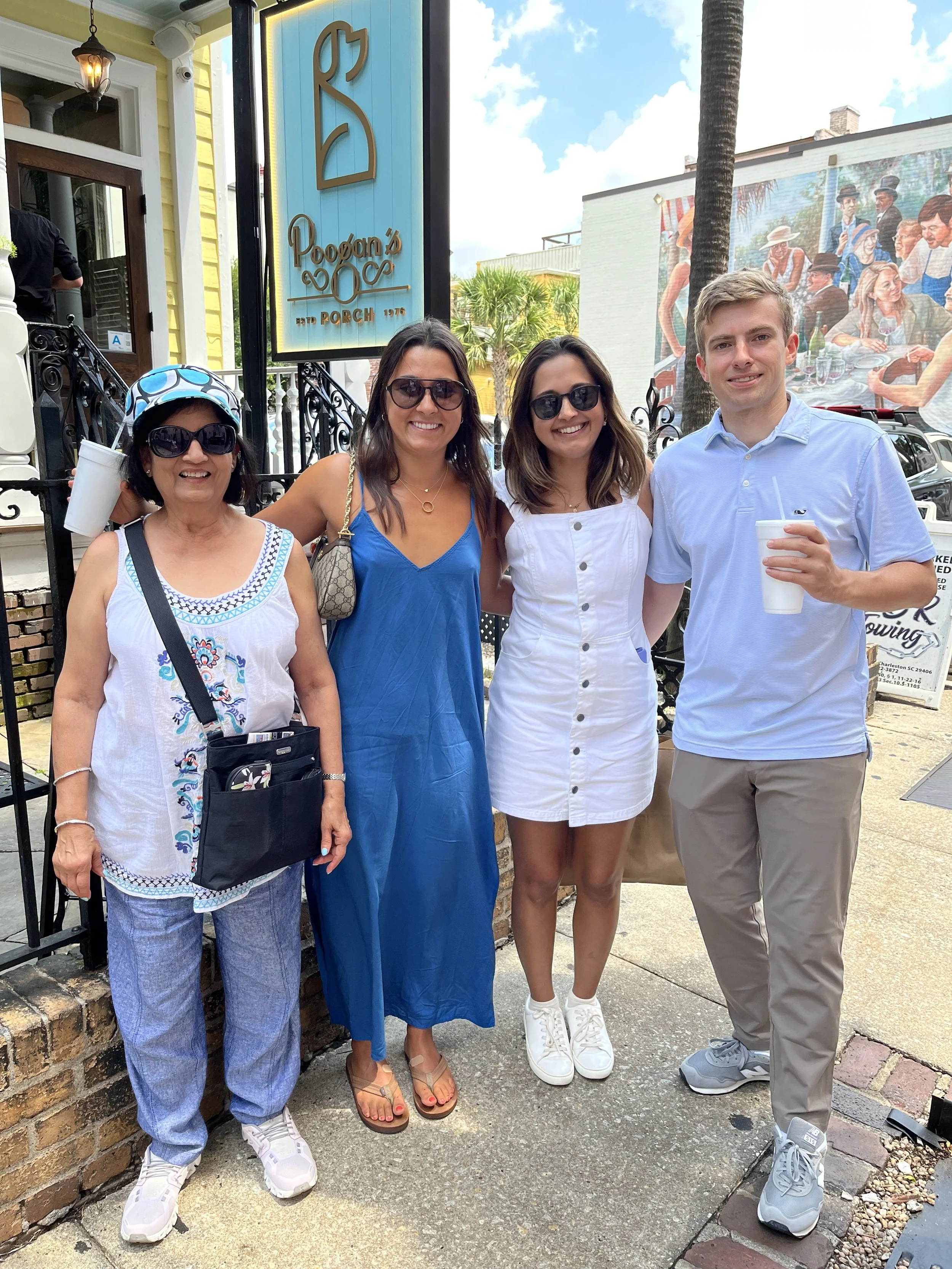 Four women and one man standing outside of Poogan's Porch restaurant, smiling and posing for the camera. The group is dressed casually, with some wearing sunglasses, and they appear to be enjoying a sunny day.