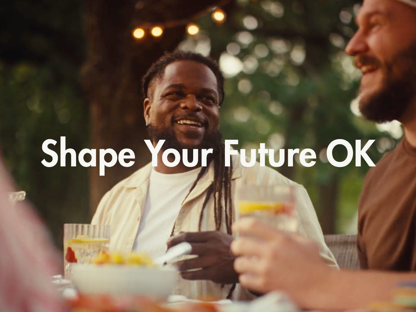 People smiling and enjoying drinks at an outdoor gathering with the text "Shape Your Future OK" overlaid.