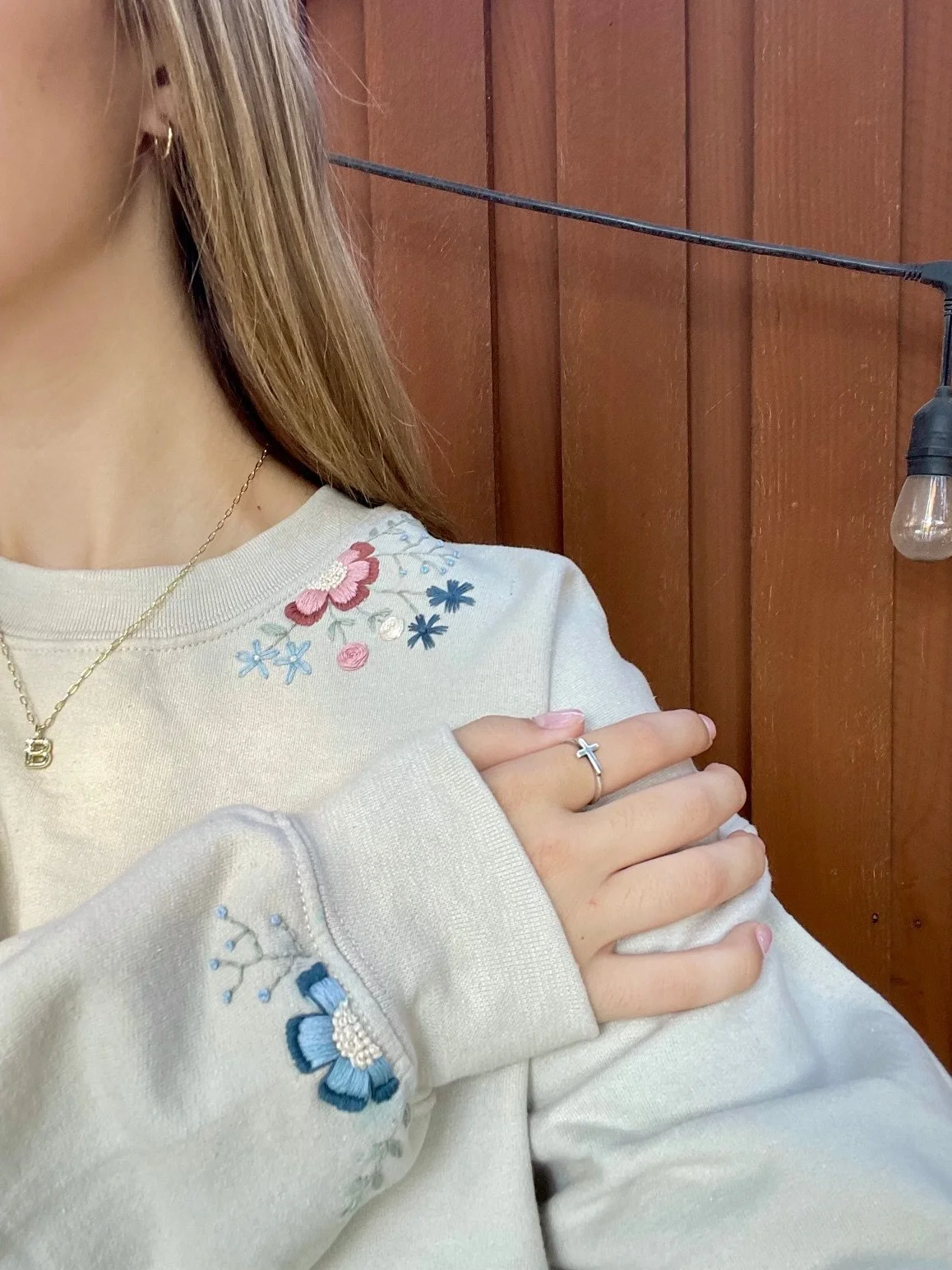 Image shows a beige colored sweatshirt with hand embroidered floral details on both the sleeve and collar.