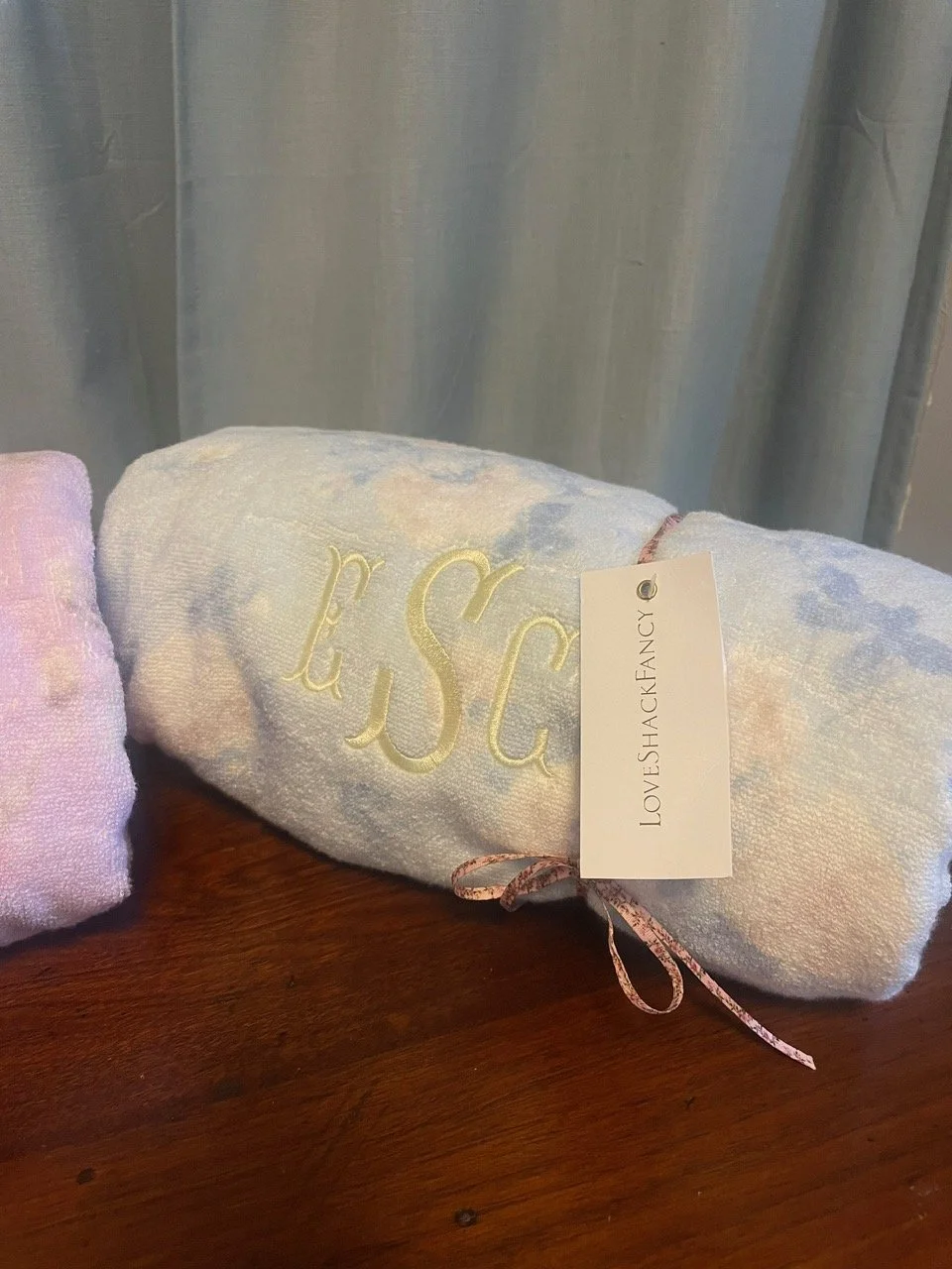 A rolled-up towel with embroidered letters 'ESC' and a label that reads 'LOVESHACKFANCY.'