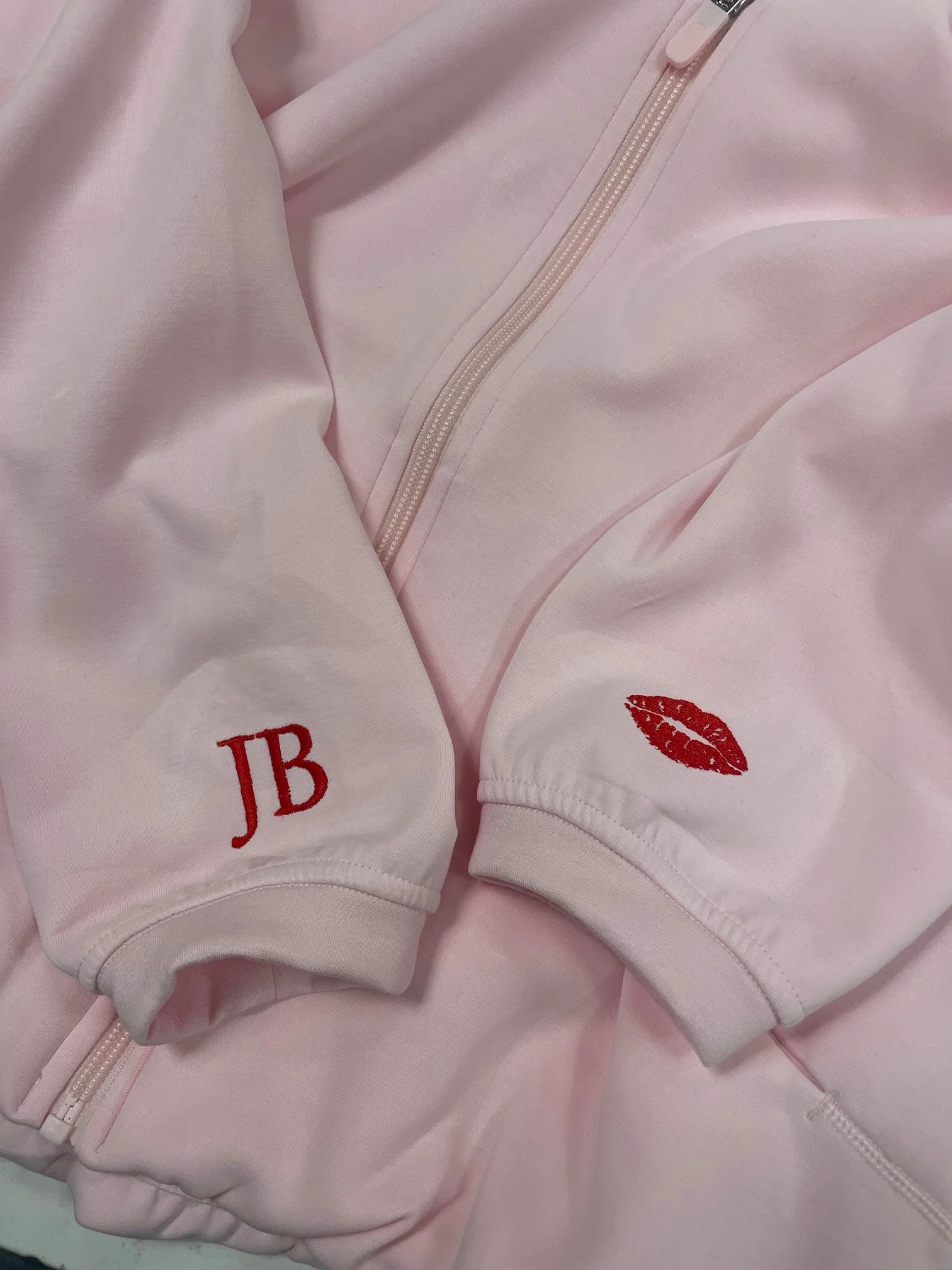 Close-up of a pink jacket with a zipper and embroidered red lips and initials 'J B' on the sleeve.
