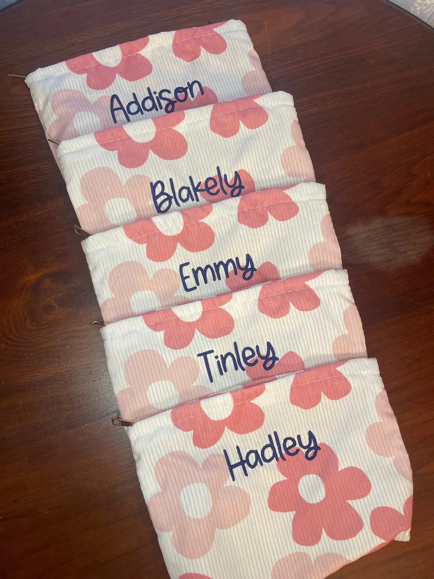 Fabric pencil case with pink and white polka dots and the names Addison, Blakely, Emmy, and Hadley embroidered in blue on pink polka dot background, placed on a wooden surface.