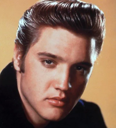 Close-up portrait of a young man with styled brown hair and serious expression, against a yellow background.