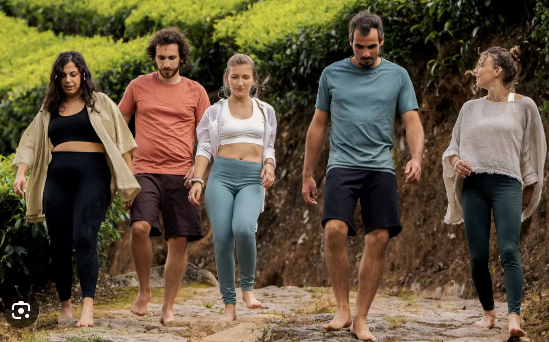 Six personnes marchant pieds nus sur un sentier en pleine nature, entourées de végétation verdoyante.