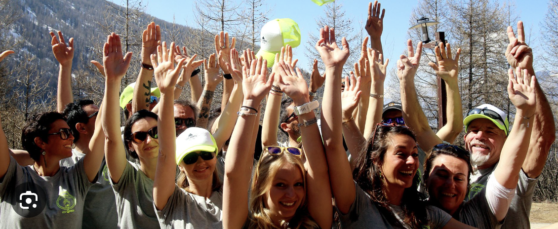 Groupe de personnes souriantes et jubiliantes avec bras levés, dehors en nature par une journée ensoleillée.