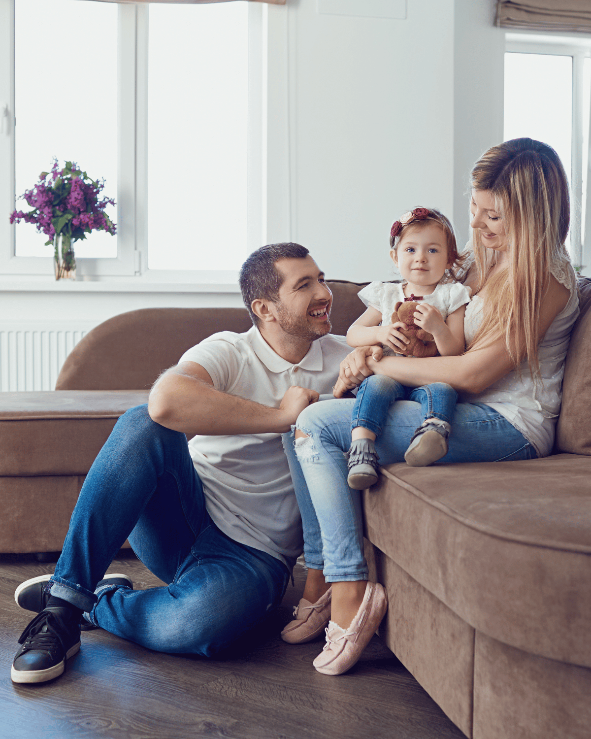 family sitting on a tan couch in front of the windows