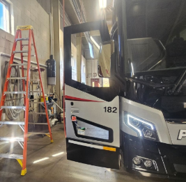Close-up of a black and white police vehicle with an open driver-side door, parked indoors with a red ladder and tools nearby.