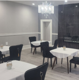 Elegant dining room with white tablecloths, black upholstered chairs, a crystal chandelier, dark accent wall, and light gray walls.
