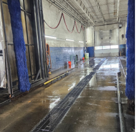 Interior of a car wash station with wet floor, drainage grate, and cleaning equipment.