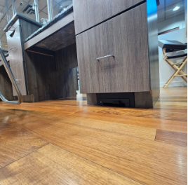 Close-up of a wooden cabinet with a vent or speaker at the bottom on a hardwood floor.