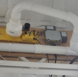 Close-up of a plumbing setup with yellow and gray equipment connected by white PVC pipes installed on a ceiling.