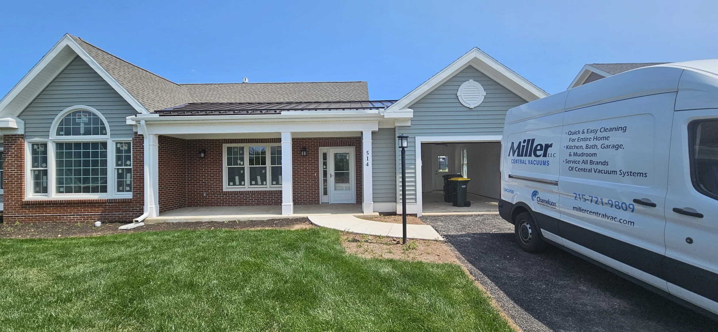 New house with gray siding, white trim, and red brick facade, with a white van labeled Miller Central Vacuums parked in driveway on a sunny day.