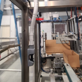 Industrial packaging or manufacturing machinery with conveyor belts and robotic arms, packing a cardboard box.