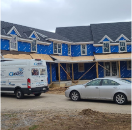 Under construction residential building with blue exterior sheathing, partially covered in plastic, with parked van and car in front.