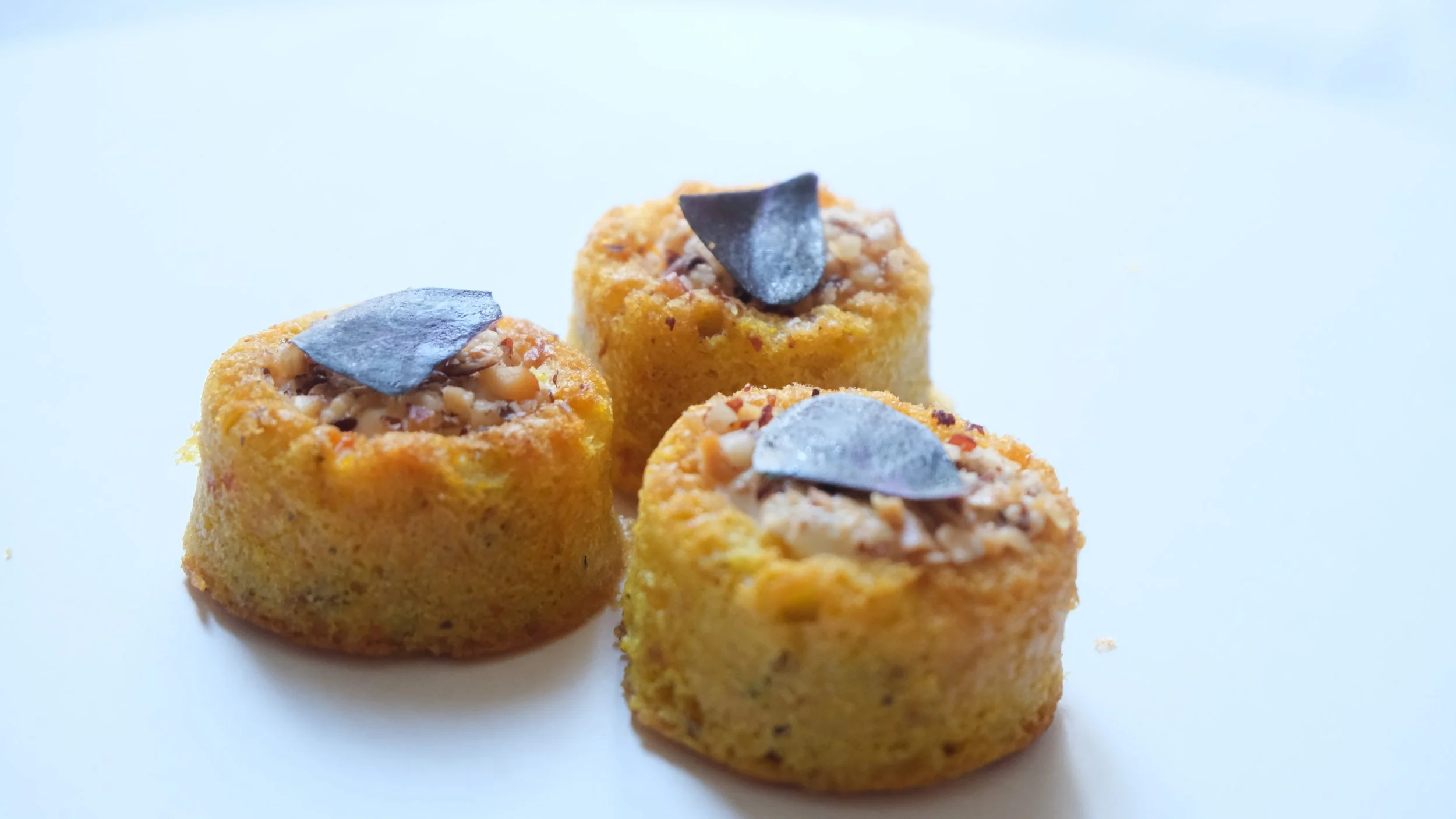 Trois petits gâteaux garnis de noix hachées et décorés d'une feuille de cacao pozée sur le dessus, sur fond blanc.