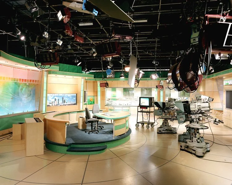 Tyler Perry Studio - Television studio set with a news anchor desk, chairs, large monitors, and camera equipment.
