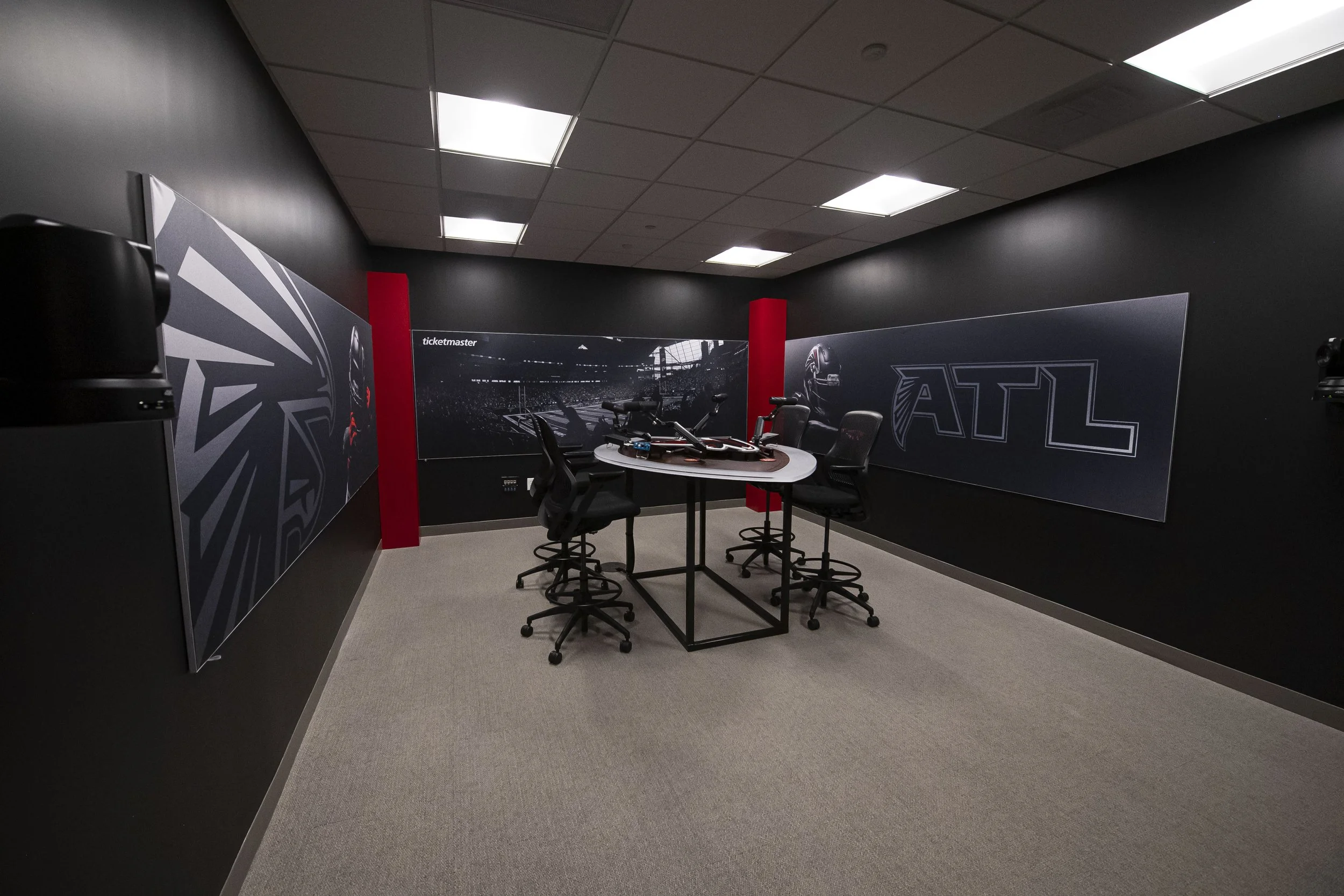 Conference room with black walls, a round table, chairs, and large sports-themed posters on the walls.
