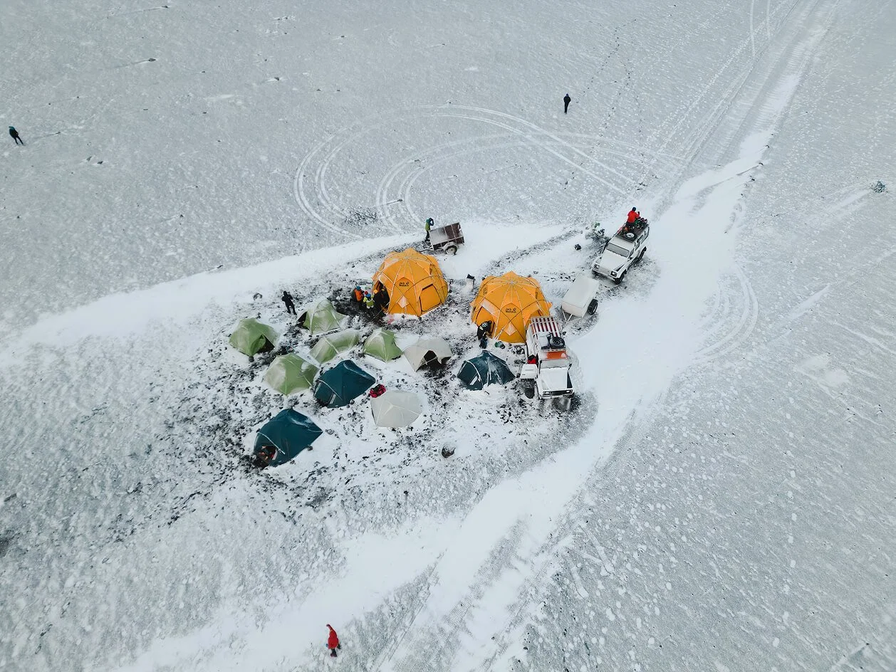 Aerial view of a snowy expedition campsite with tents and 4x4 vehicles in Iceland
