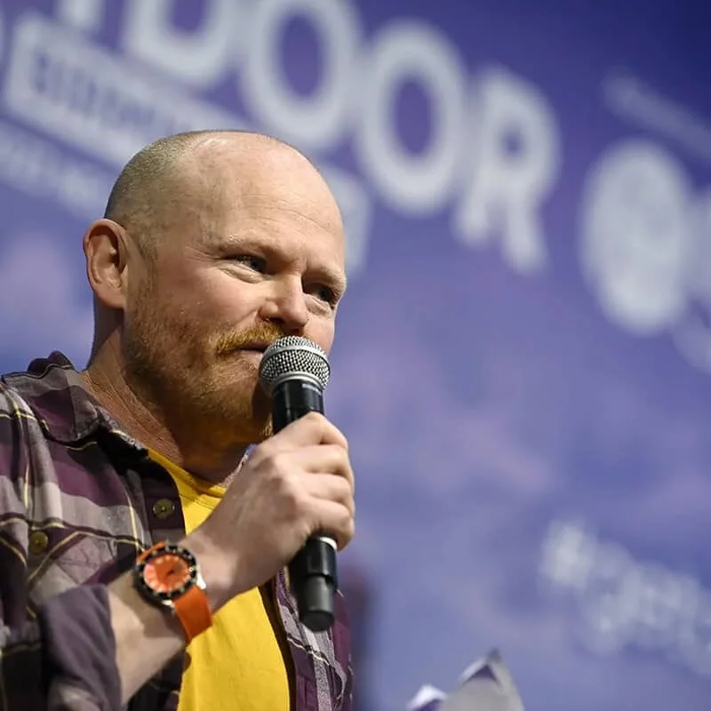 Danny Bent speaking on stage into a microphone during a live event