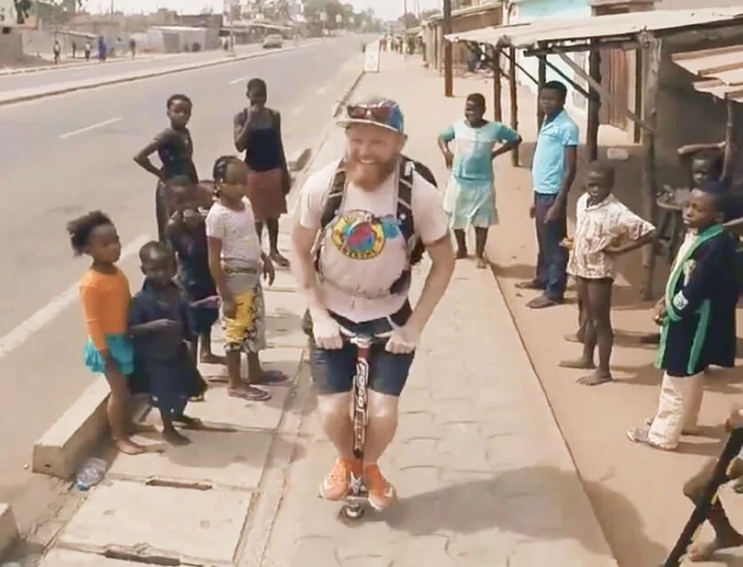 Danny Bent riding a pogo stick on a street in Togo surrounded by children