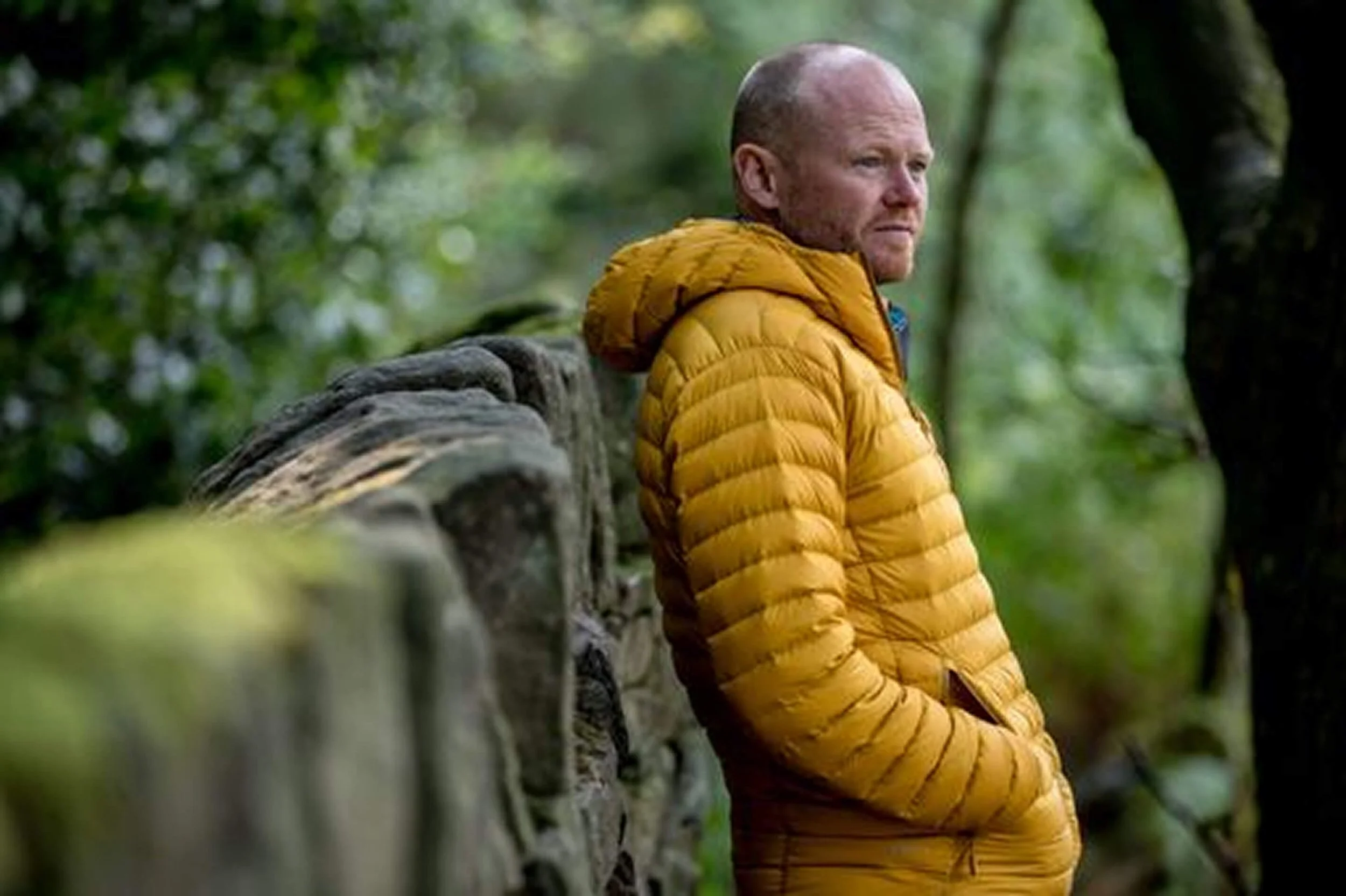 Danny Bent wearing a yellow puffer jacket leaning against a tree