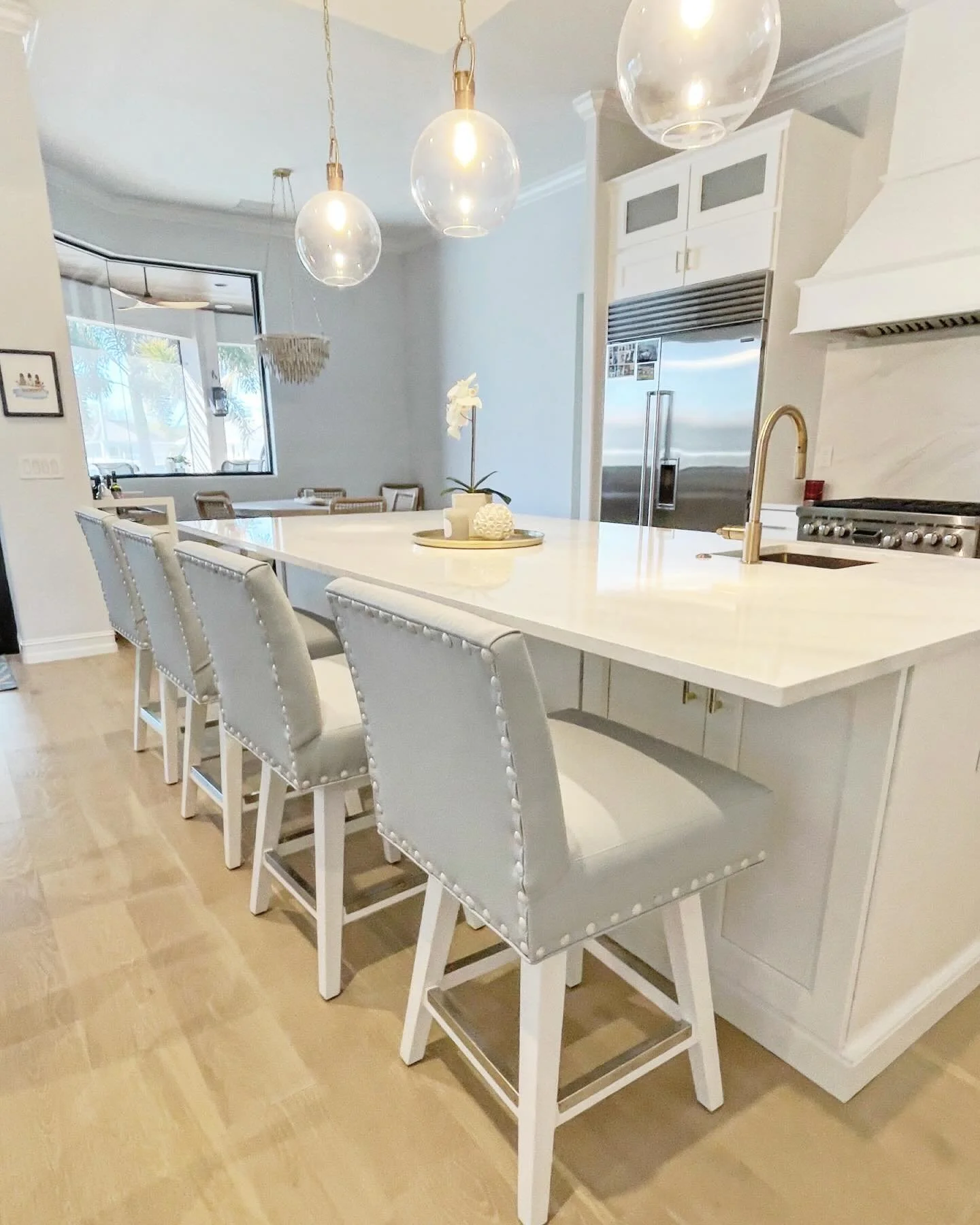 Quiet coastal, done right.
A coastal modern kitchen layered in crisp white quartz and clean lines, paired with swivel bar stools in soft blue performance leather.  The subtle nailhead detail adds just the right touch of polish&mdash;airy, timeless, a