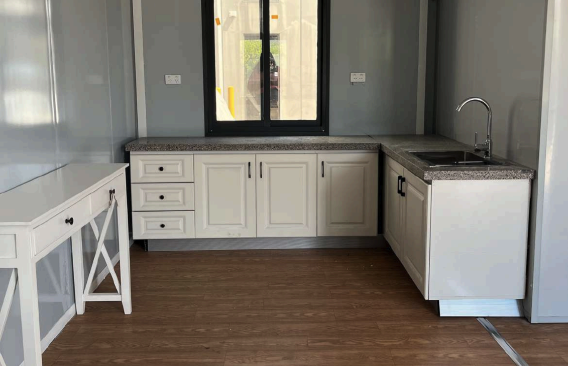 Kitchen with white cabinets, granite countertops, a sink, and a window facing outside, with wooden flooring