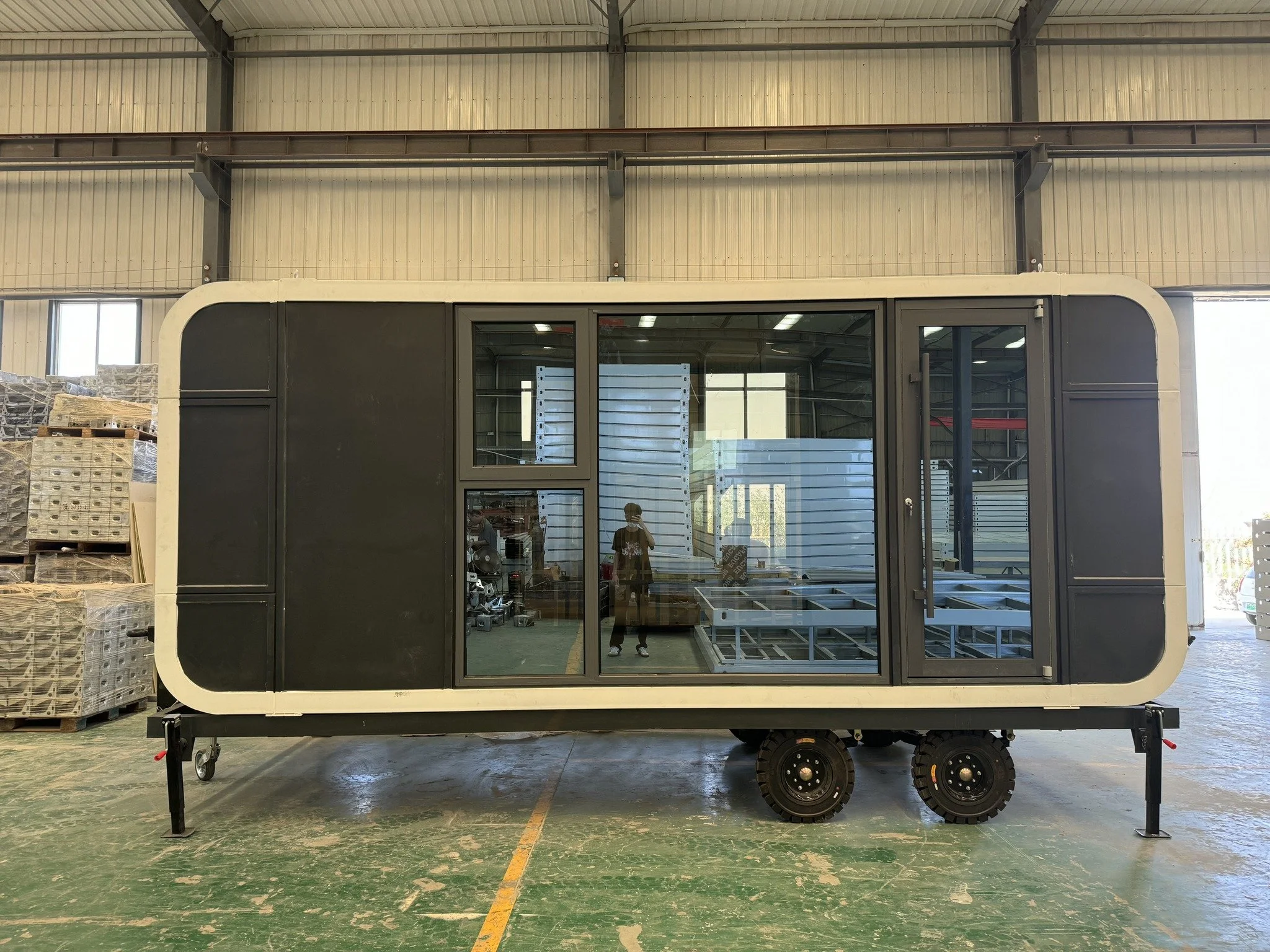 A mobile kiosk with glass windows and a black exterior, situated inside a large industrial warehouse with pallets of goods nearby.
