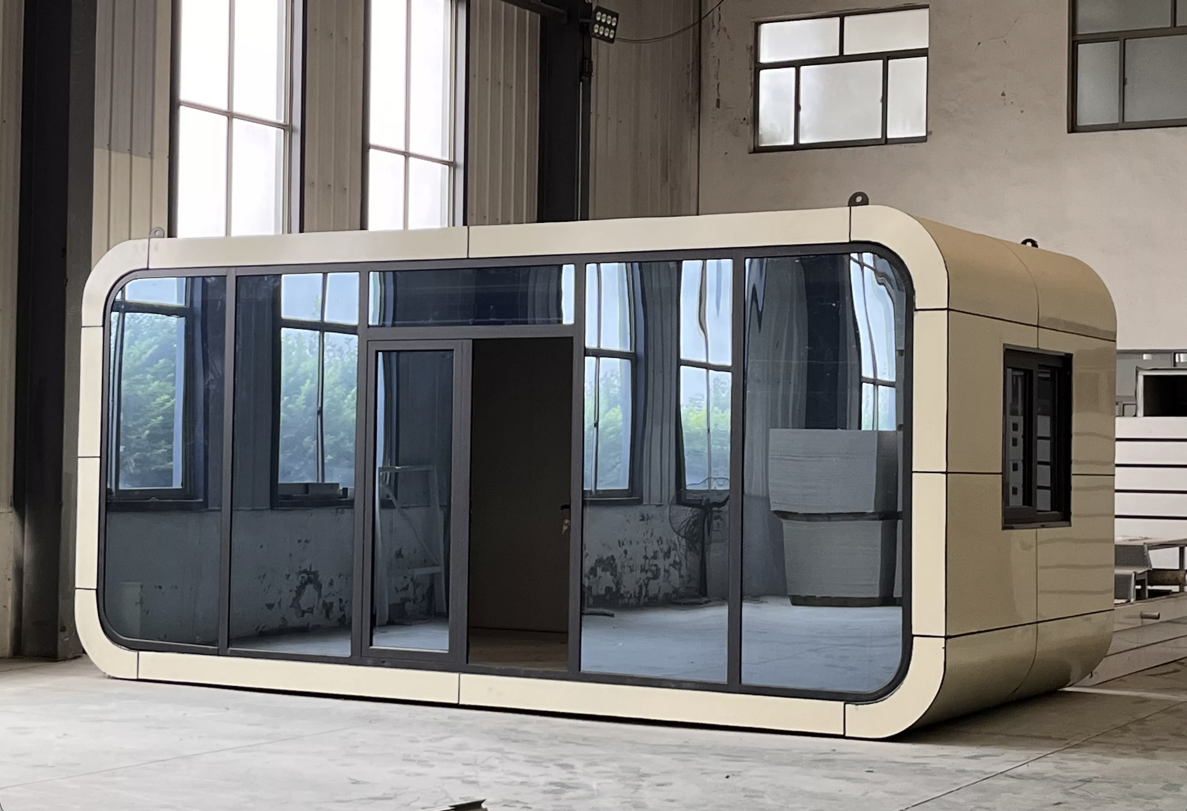 A modern interior space with large glass windows and a unique capsule-shaped structure with a curved metallic exterior and transparent glass panels, under construction or renovation.