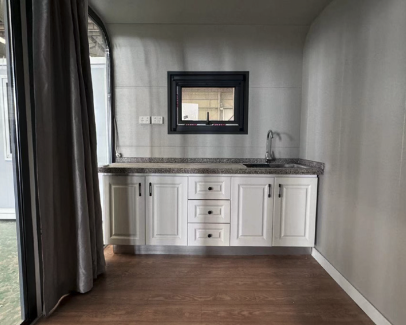 Small kitchen with white cabinets, granite countertop, and a small sink, featuring a window and electrical outlets on the wall.