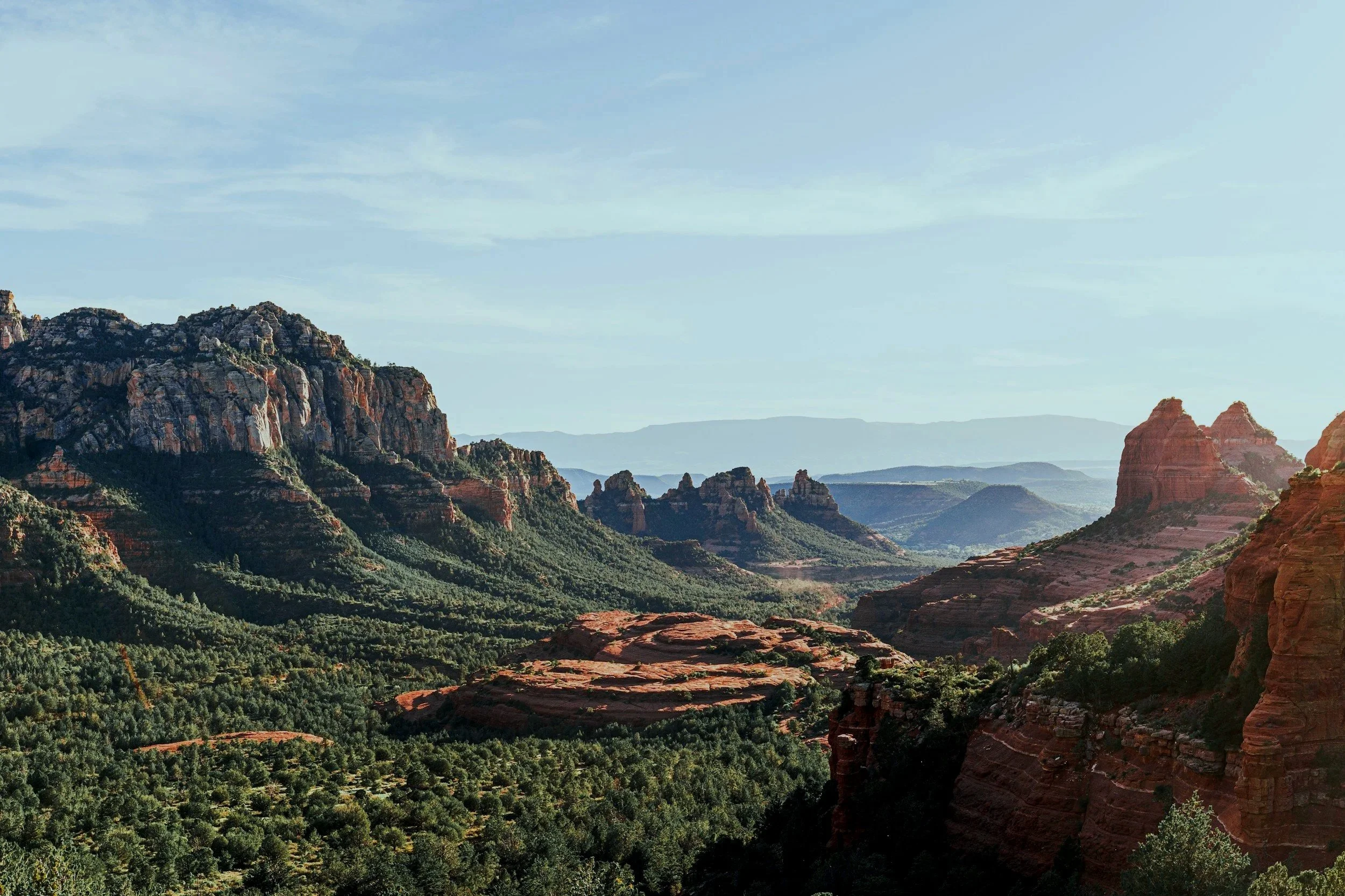 Scenic view of the red rocks of Sedona with lush green landscape and a clear sky.