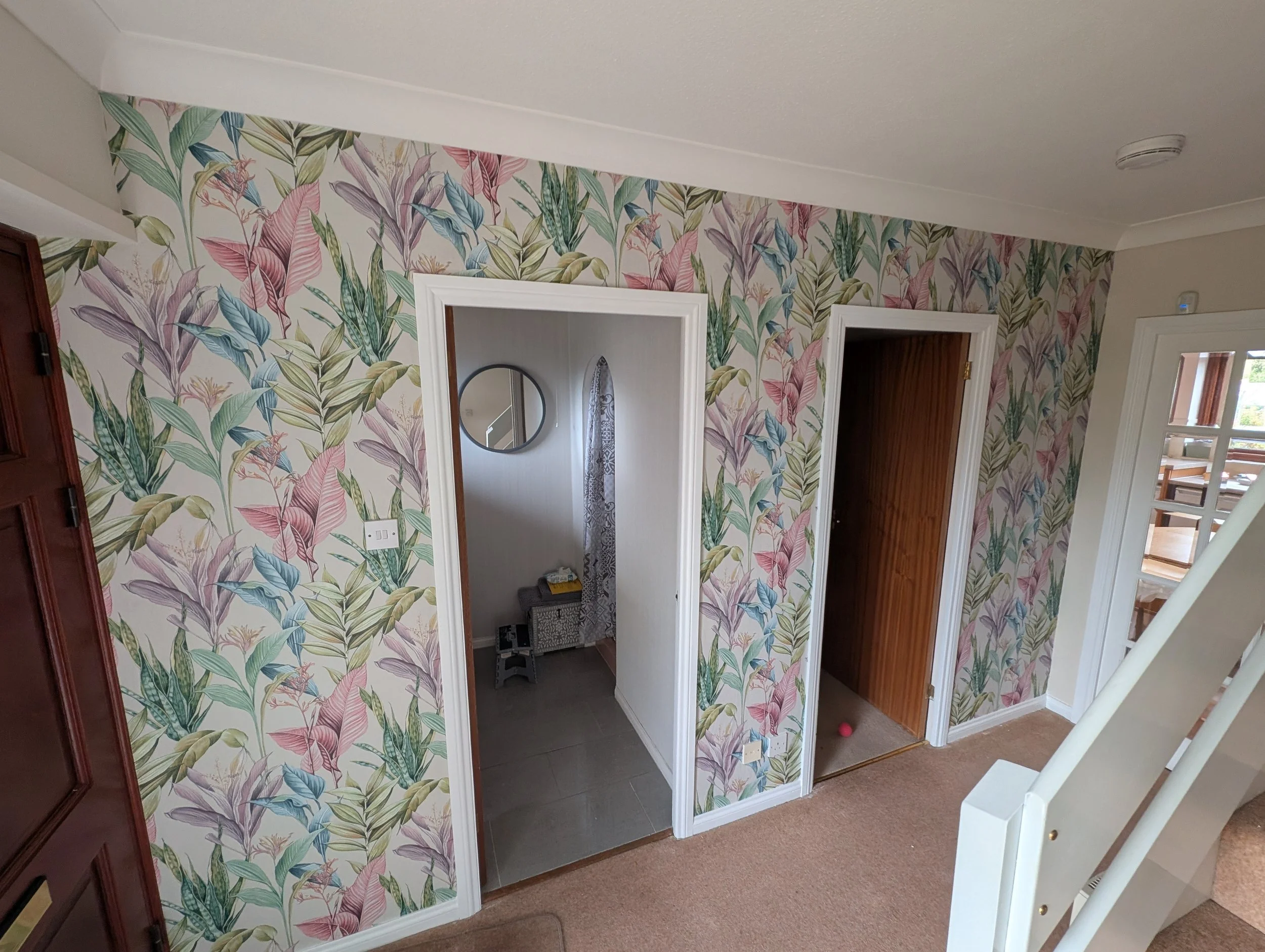 Interior of a home with floral wallpaper, showing doorways leading to a bathroom and another room, with staircase on the right.