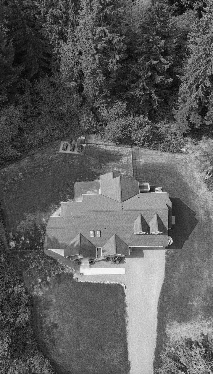 Aerial view of a house with a yard and trees surrounding it, taken from above.