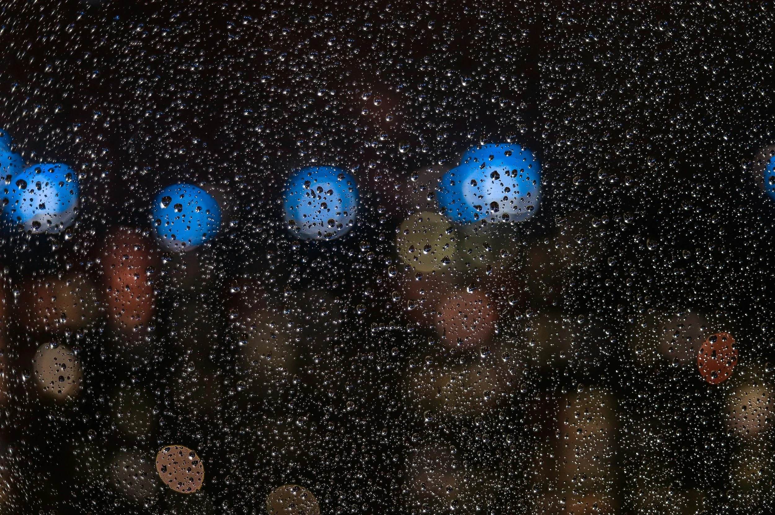 Rain droplets on a window with blurred city lights in the background at night.