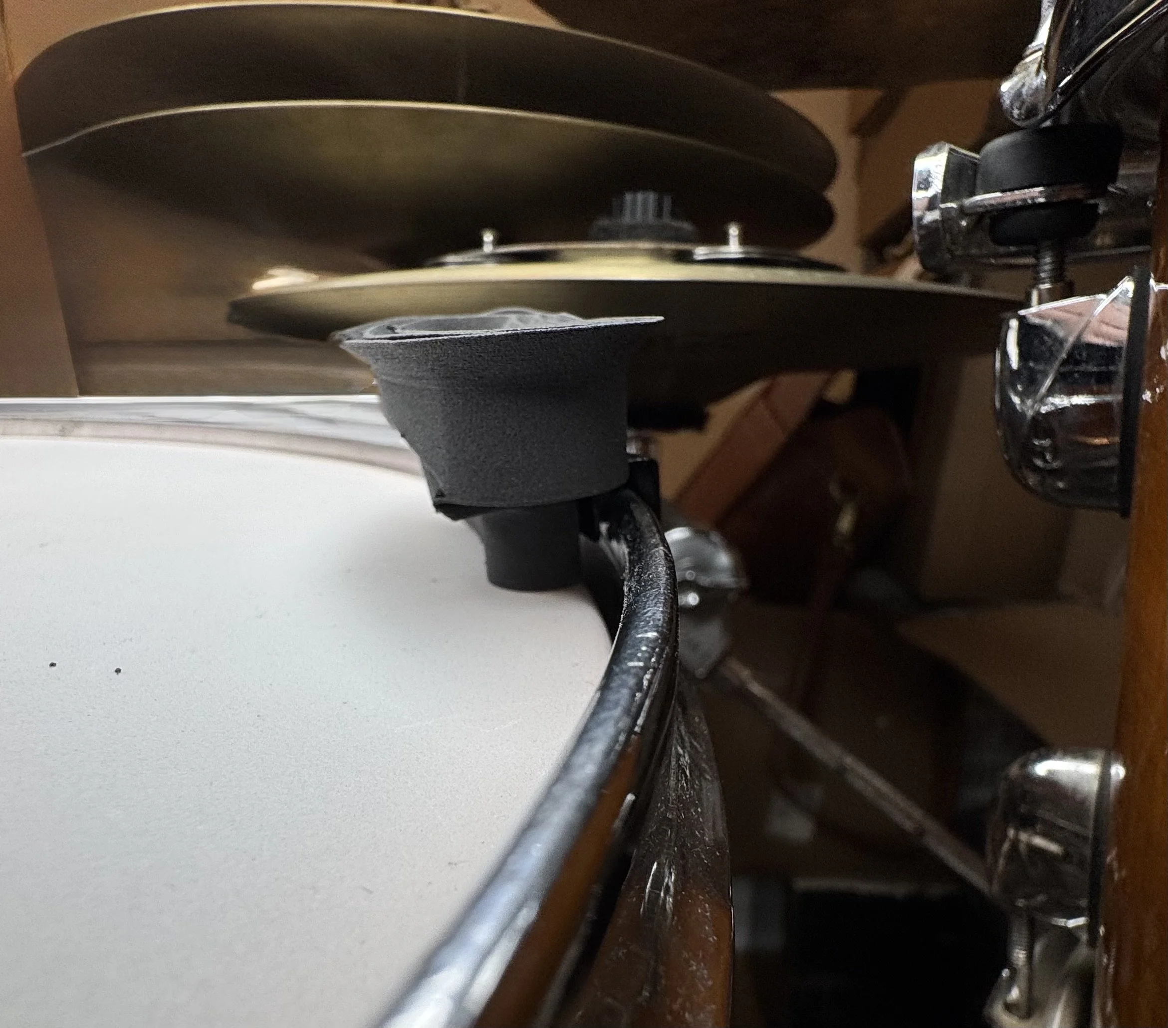 Close-up of a snare drum's side and drum hardware in a drum kit, with several cymbals in the background.