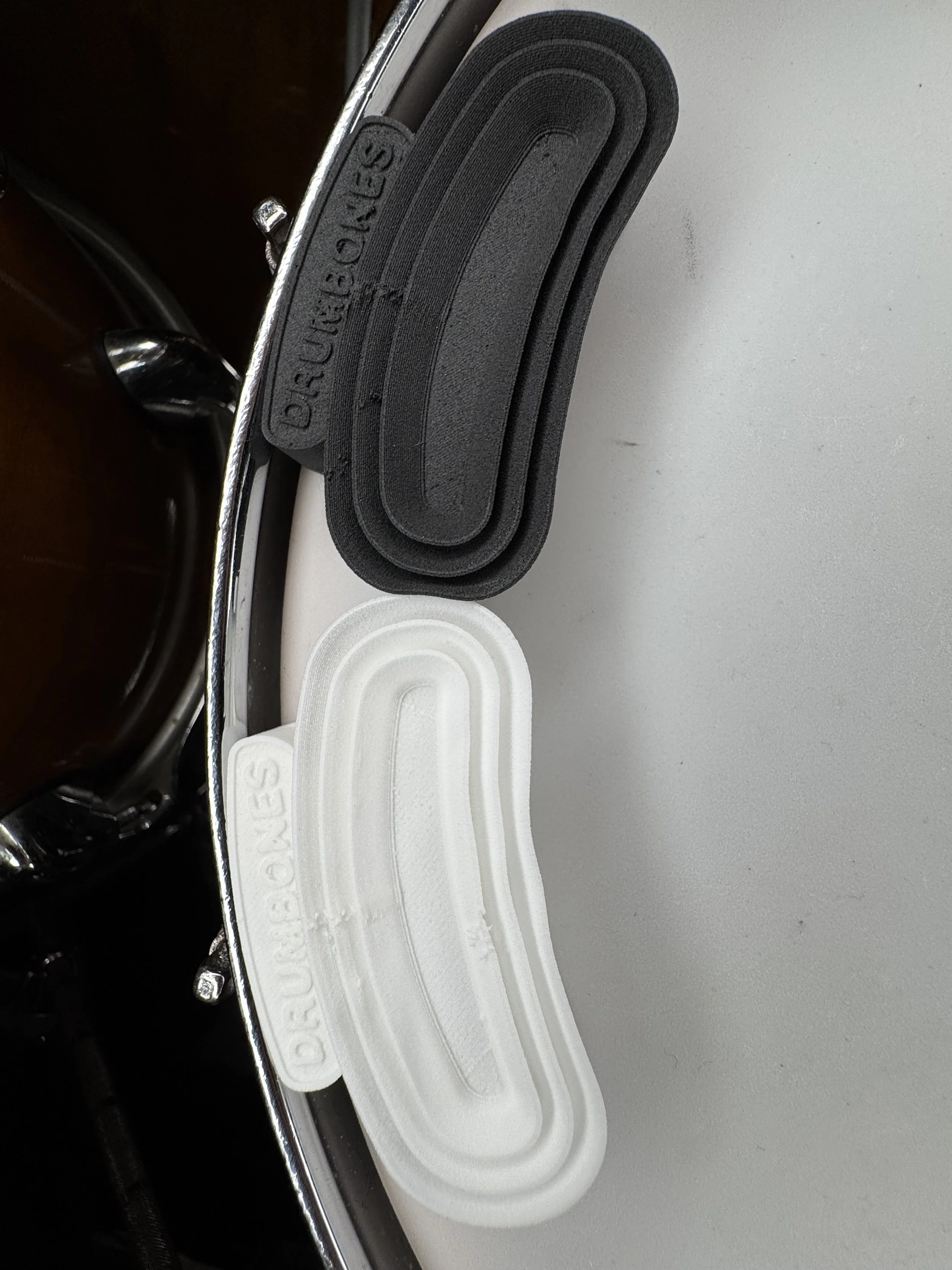 Two pairs of foam earplugs, one black and one white, placed on a white surface near a chrome edge of a table or frame.