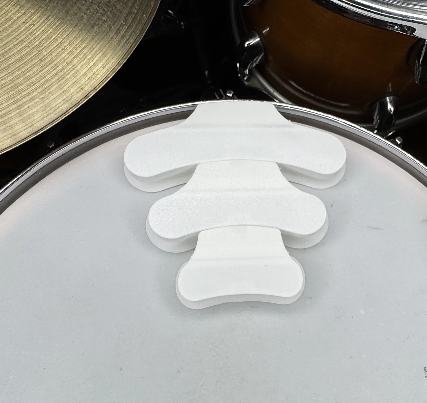 Close-up of three white foam pads on a drum's surface, with different drums partially visible in the background.