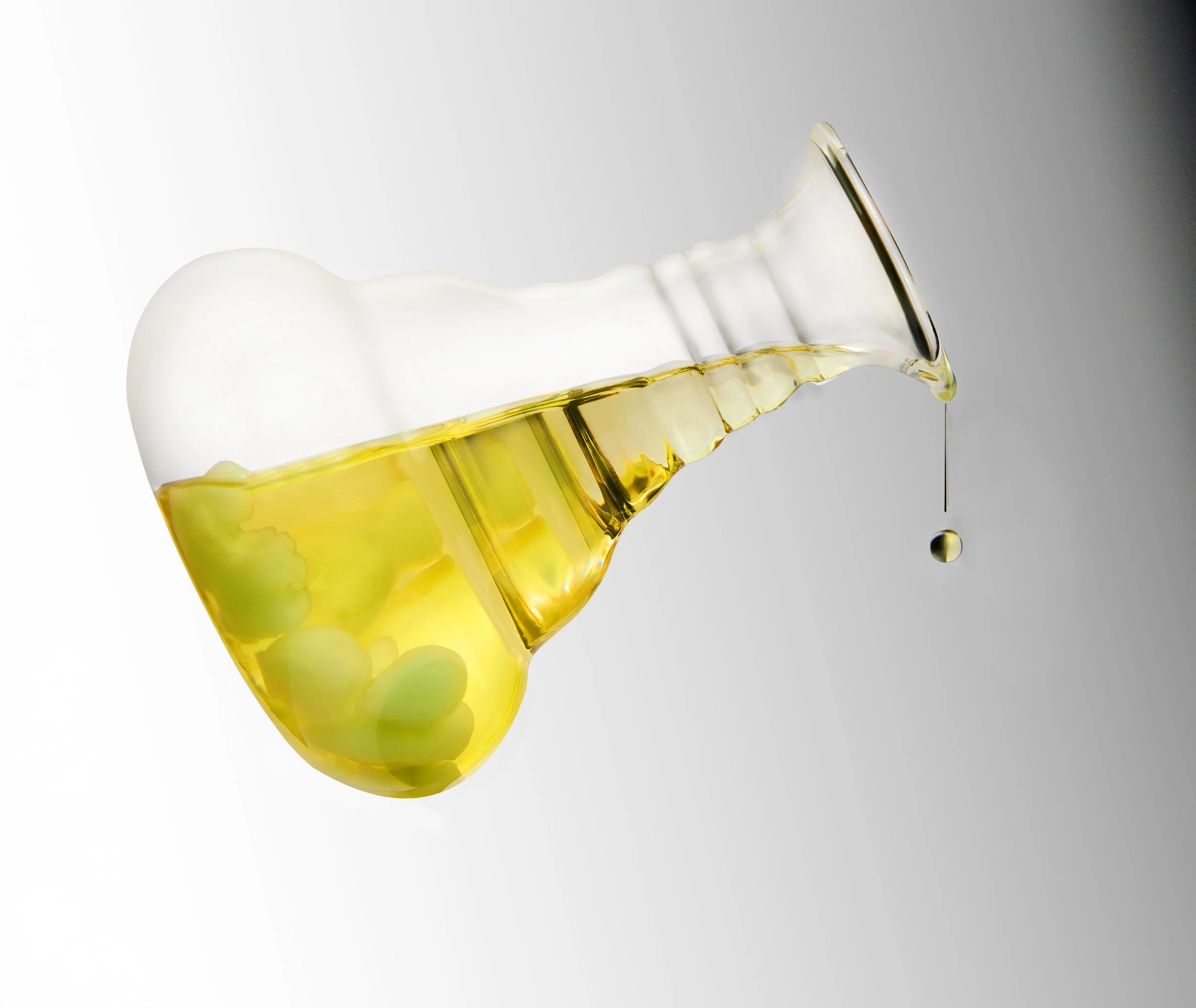 A glass of white wine with green grapes inside, spilling over the edge with a drop falling from the rim, against a plain background.